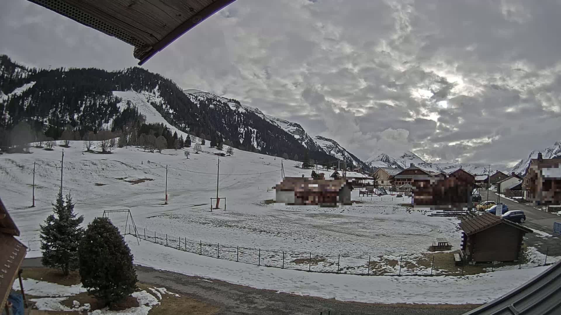A snow-covered village nestled in a valley between mountains under a cloudy sky.