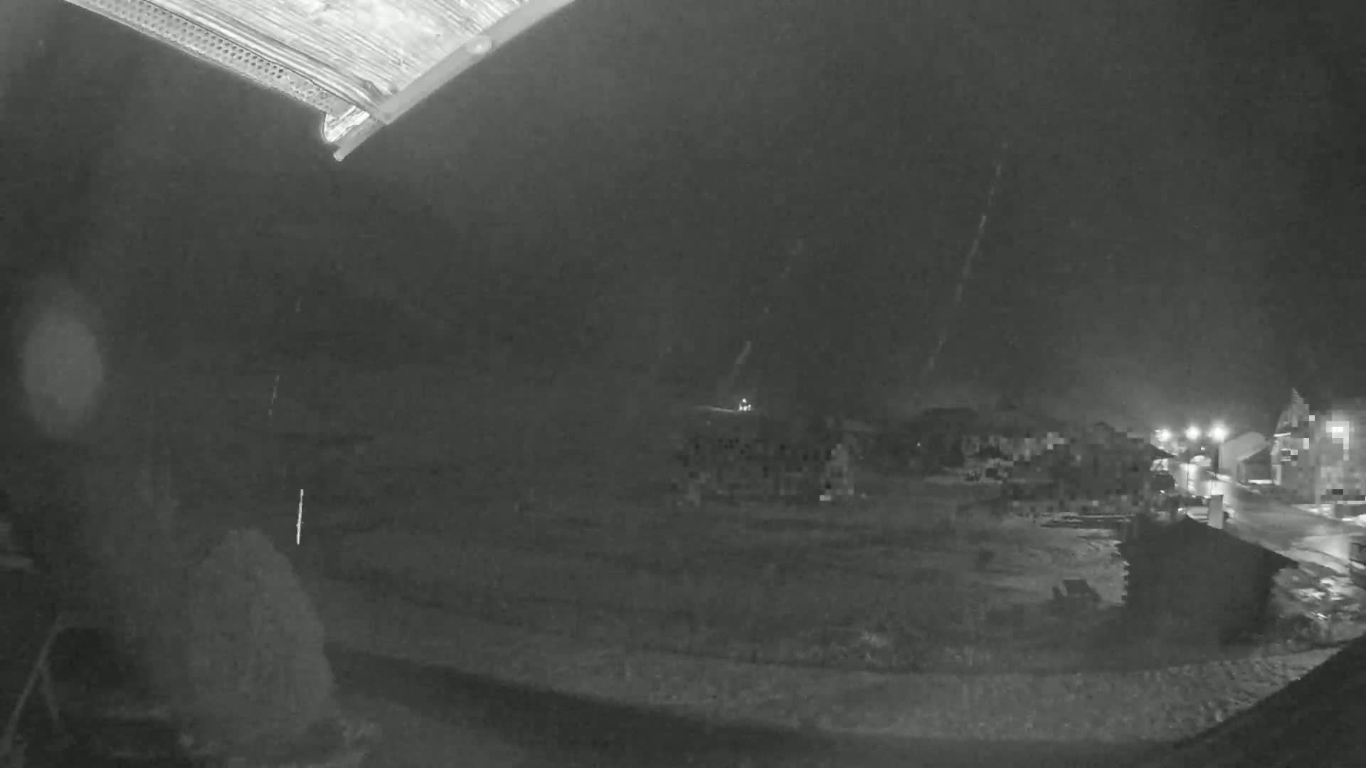 A nighttime view shows light snow falling over a residential area with several buildings visible in the distance.