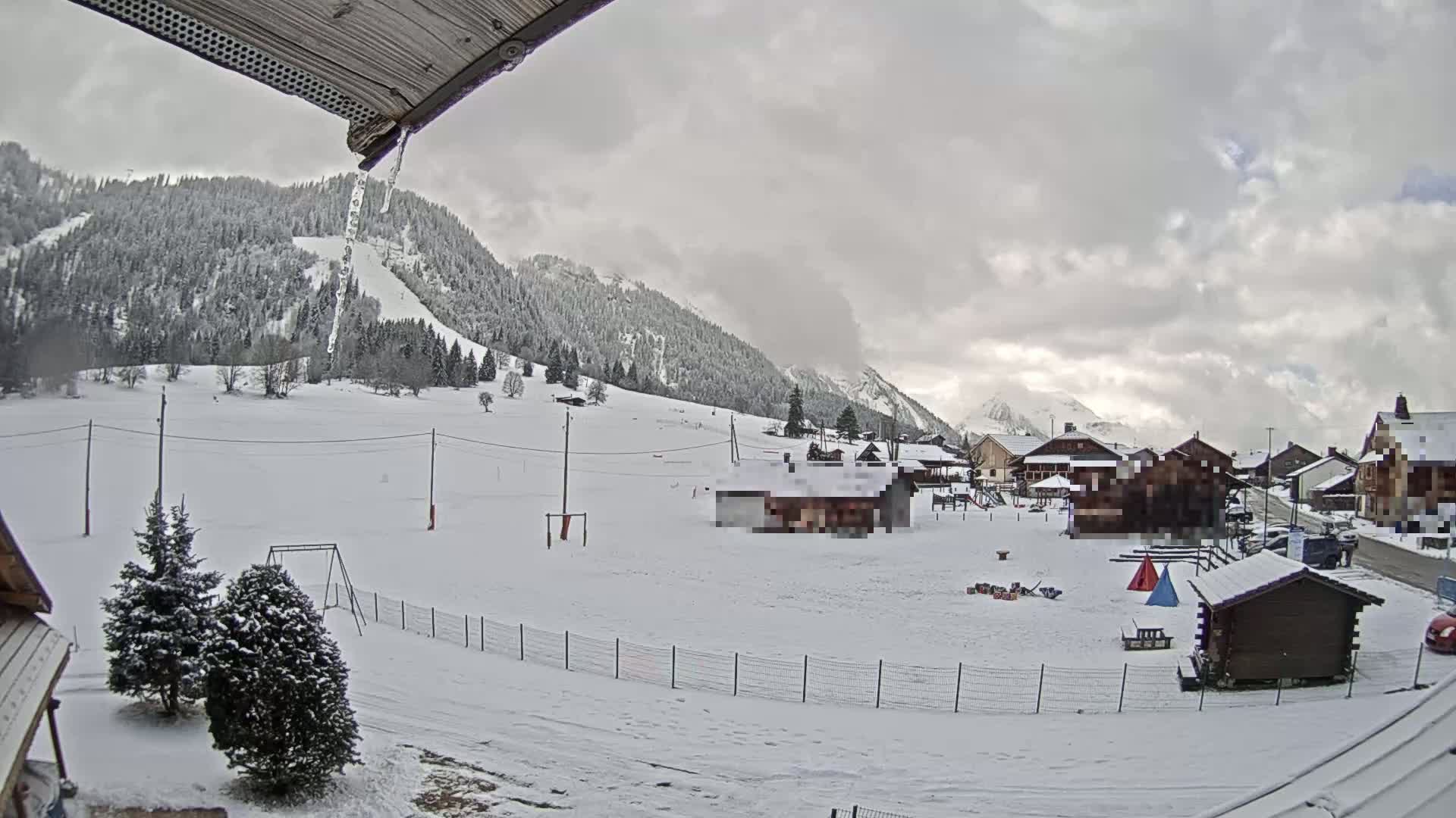 A snow-covered village nestled in a valley between snow-covered mountains under an overcast sky.