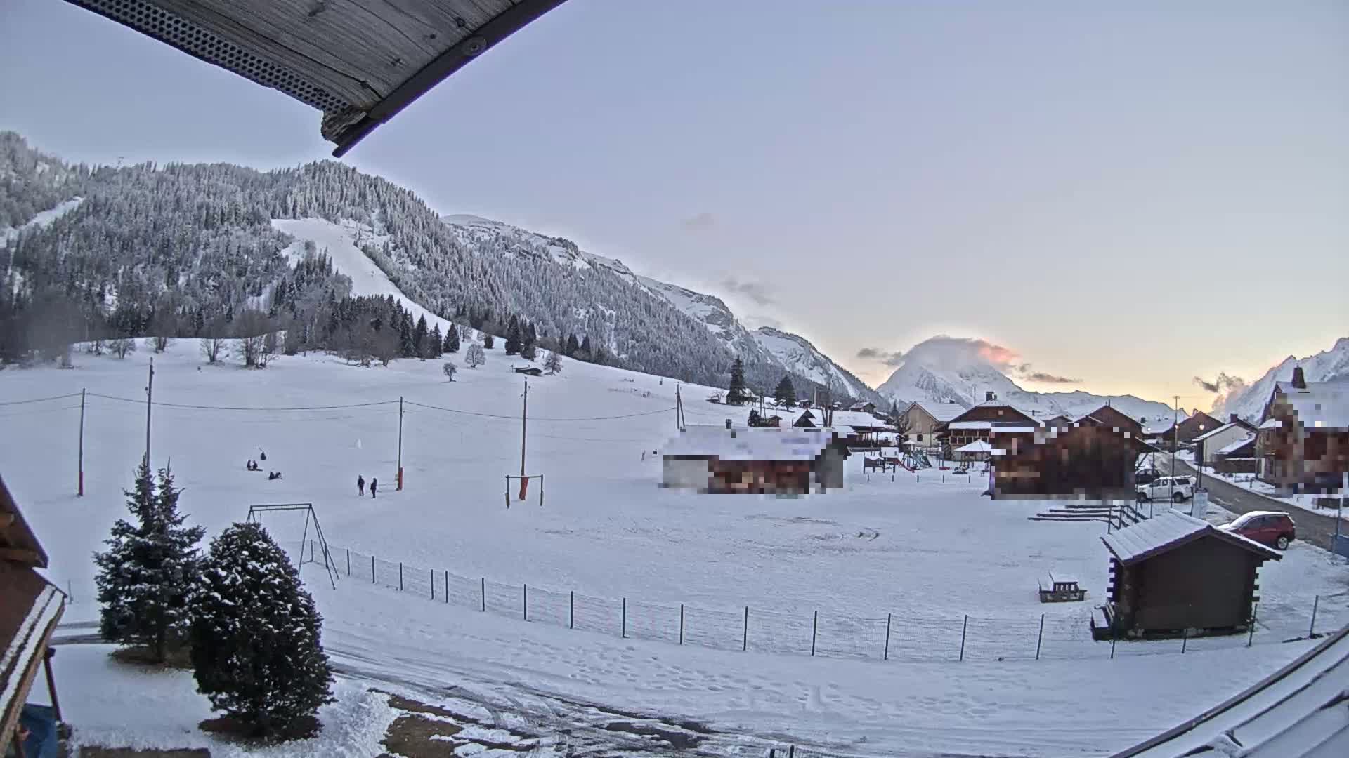 A snow-covered village nestled in a valley between snow-dusted mountains at sunrise.
