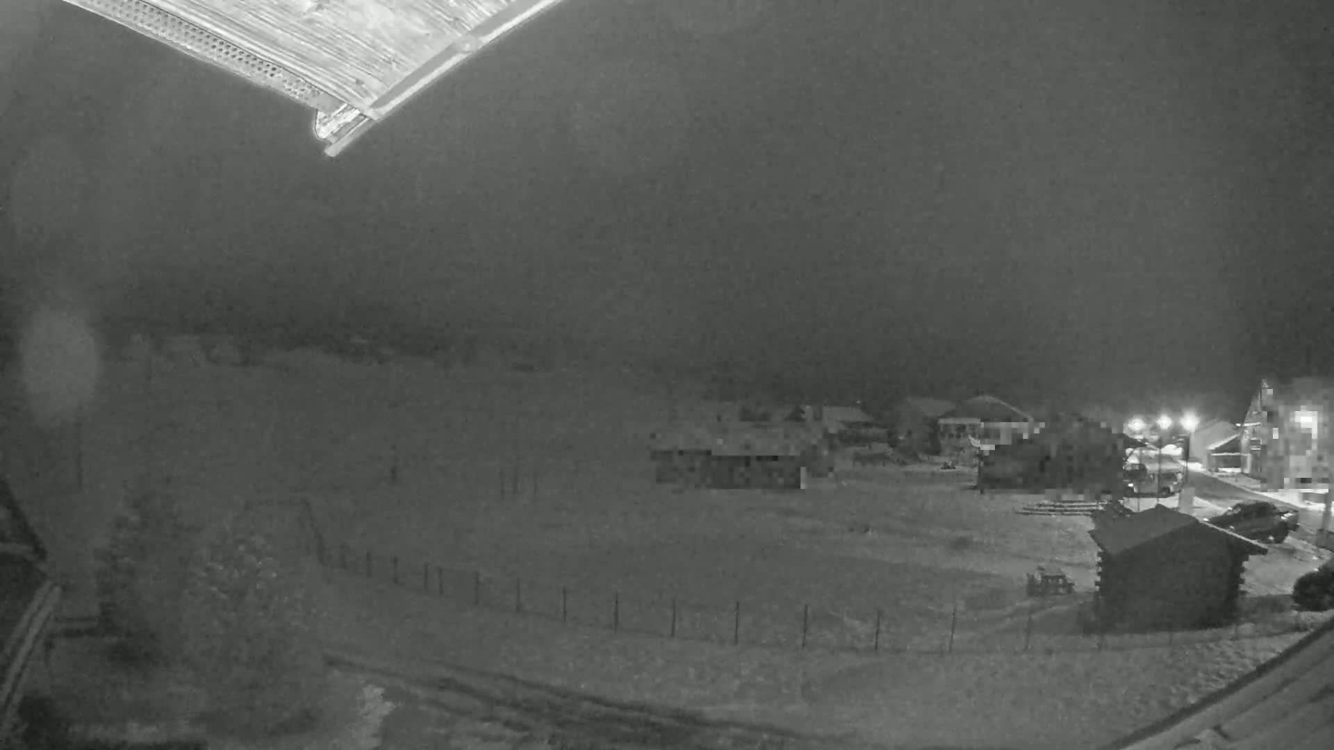 A nighttime, snow-covered scene shows several buildings and a few vehicles under a dark, overcast sky.