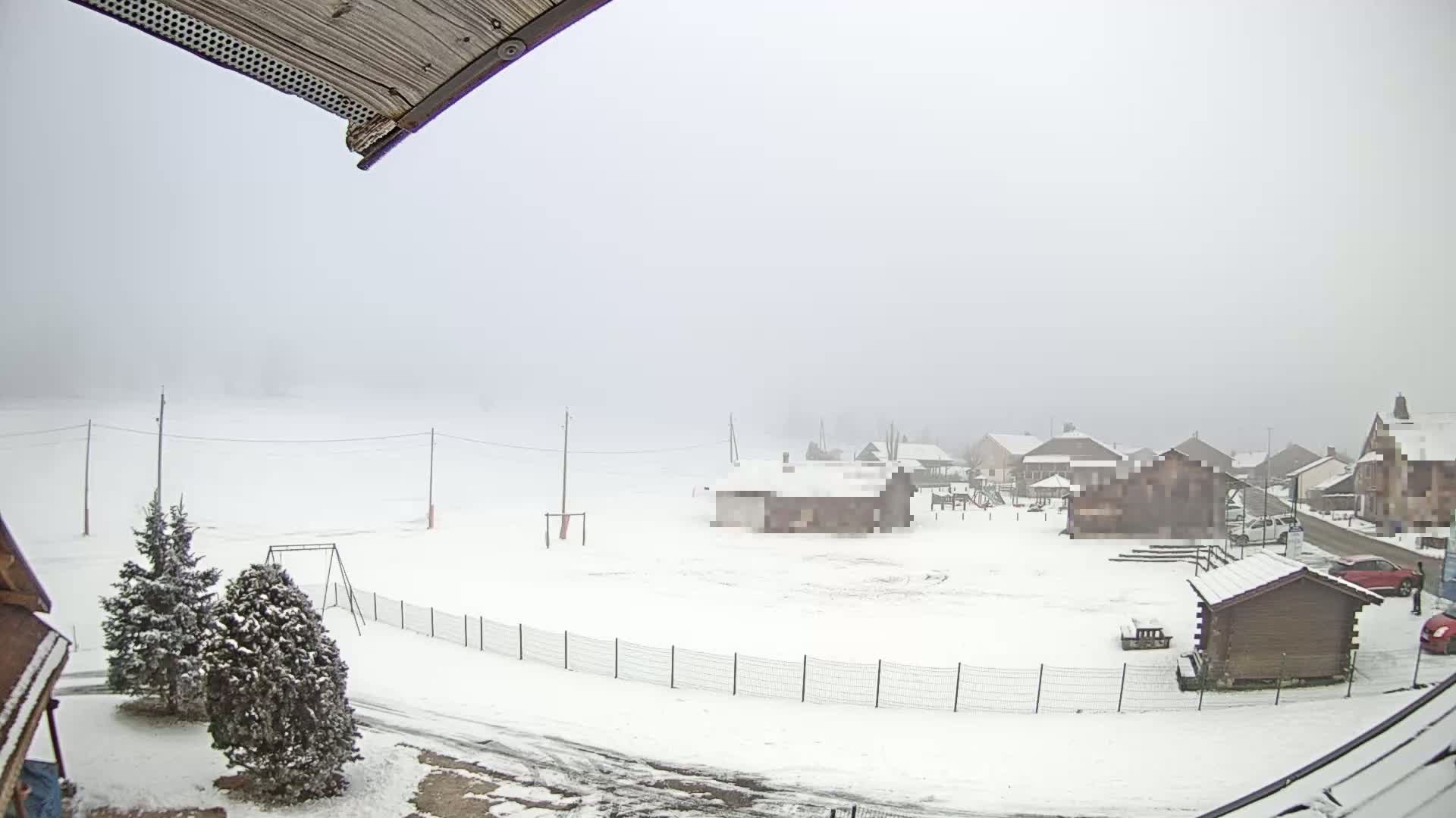 A snow-covered landscape with several buildings and a playground is visible in foggy conditions.