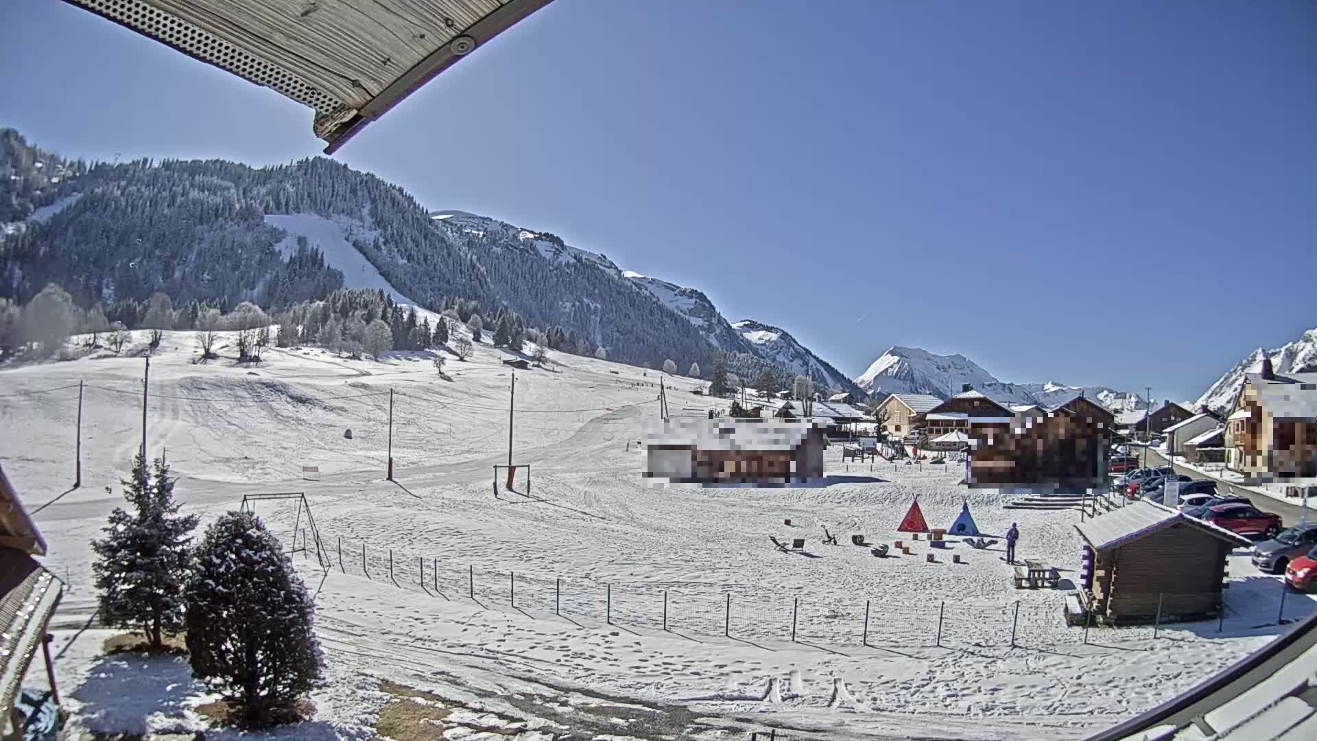 A snow-covered mountain village with a children's play area, under a clear blue sky.