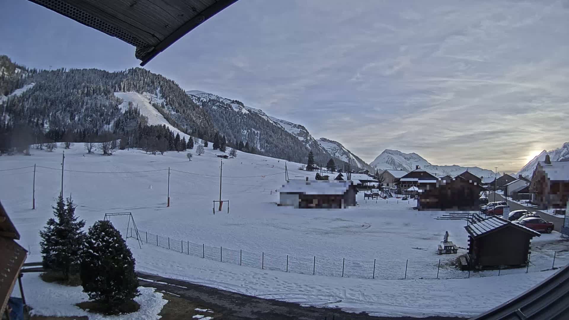 A snow-covered valley with a small village nestled amongst snow-capped mountains under a mostly clear, twilight sky.