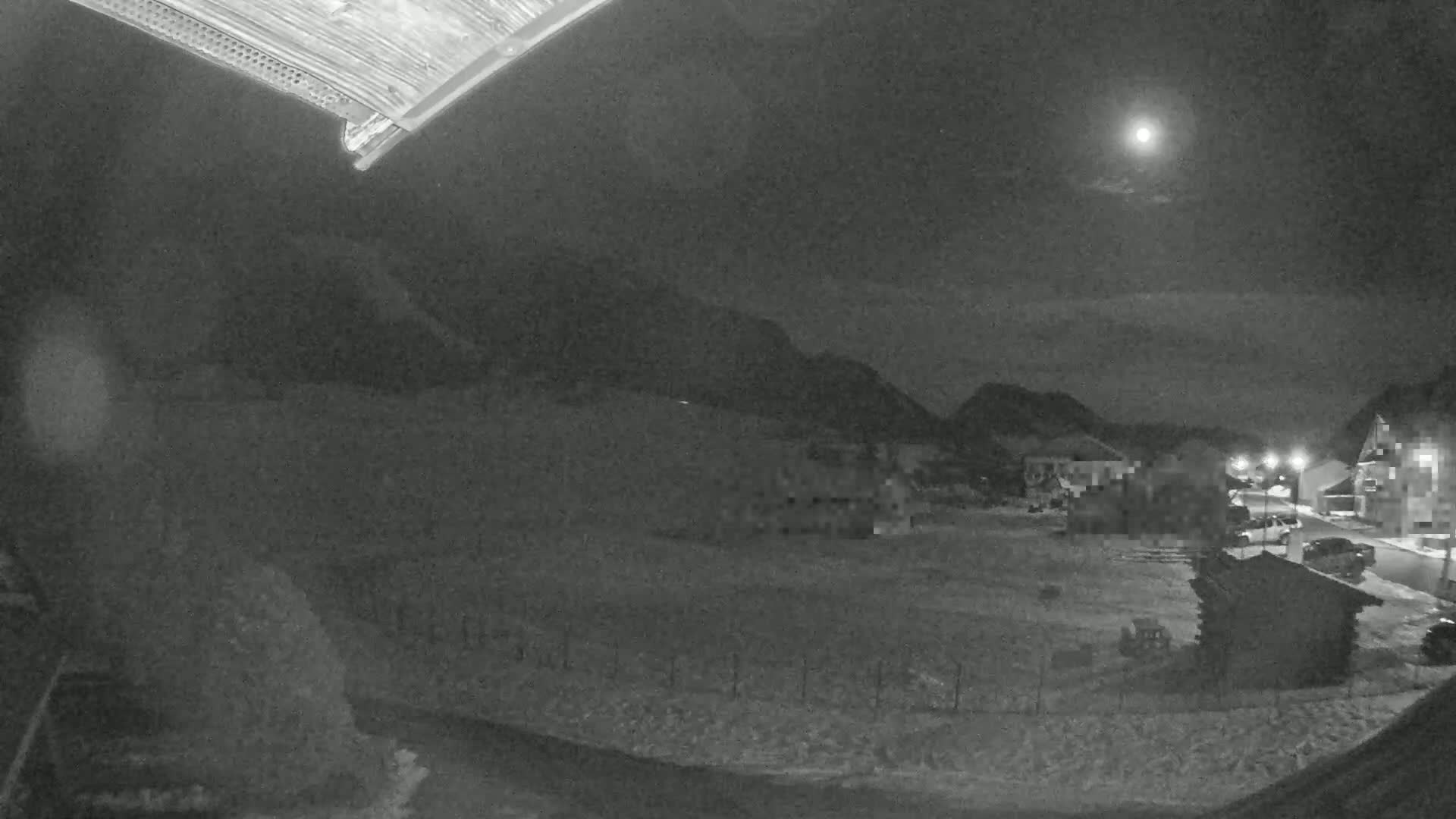 A nighttime view of a snow-covered area with buildings and a bright moon in the sky.
