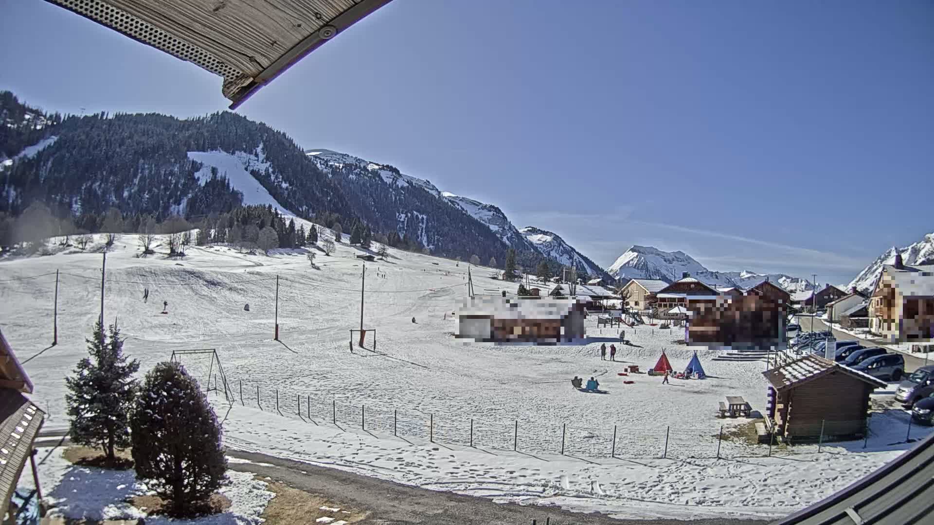 A snow-covered landscape with a small village nestled at the base of snow-capped mountains under a clear blue sky.