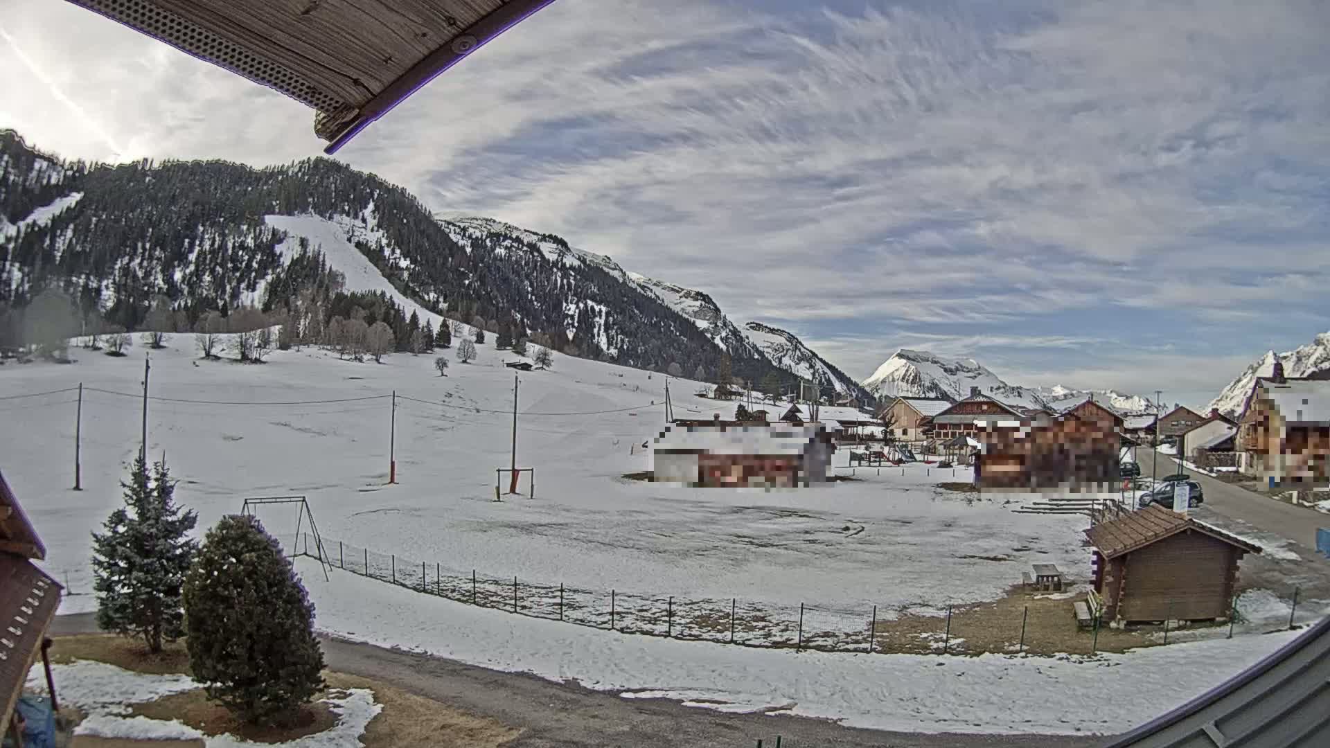 A snow-covered village nestled in a valley between mountains under a partly cloudy sky.