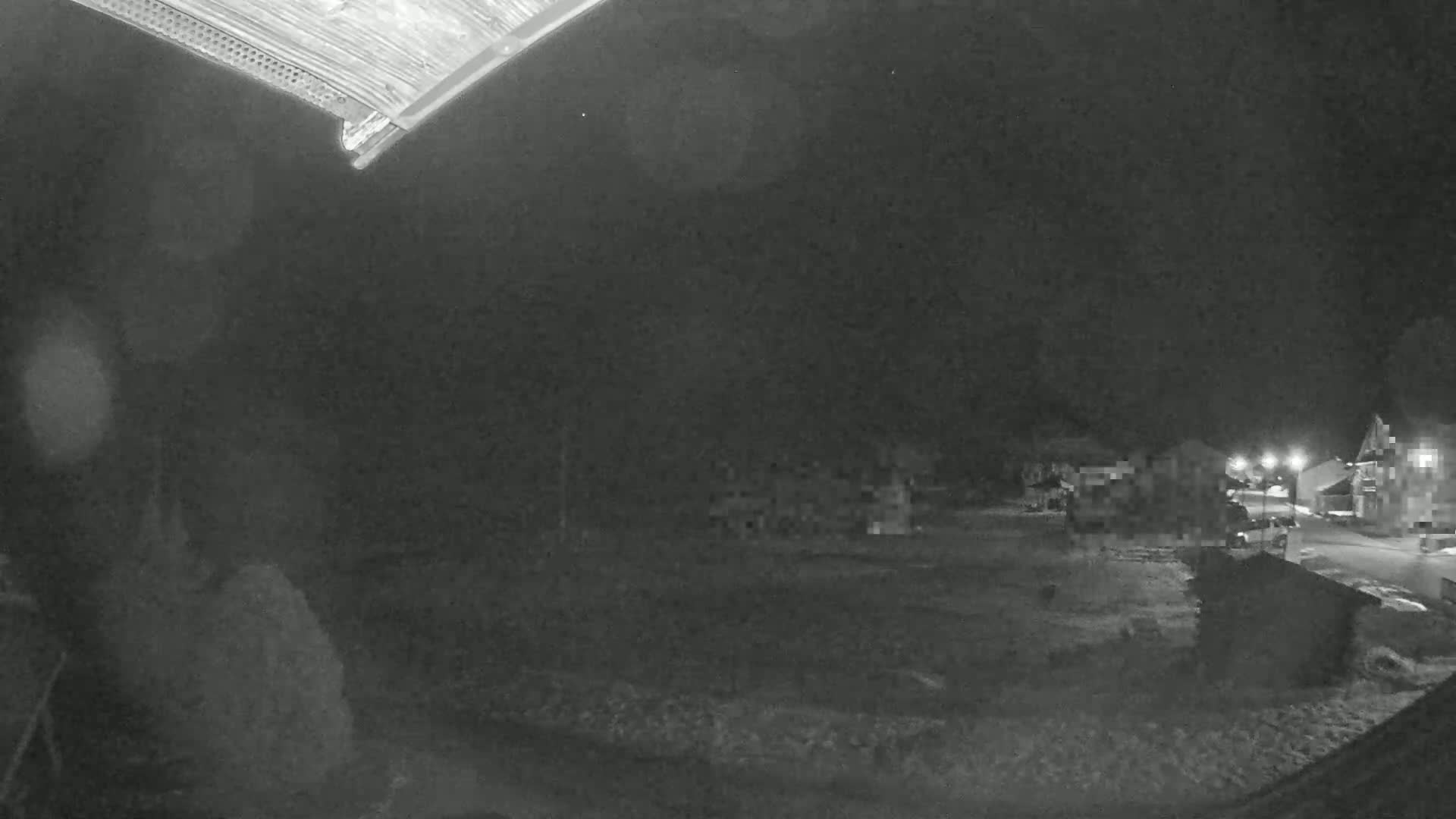 A nighttime, low-light view of a snow-covered residential area with dimly lit buildings and a street.