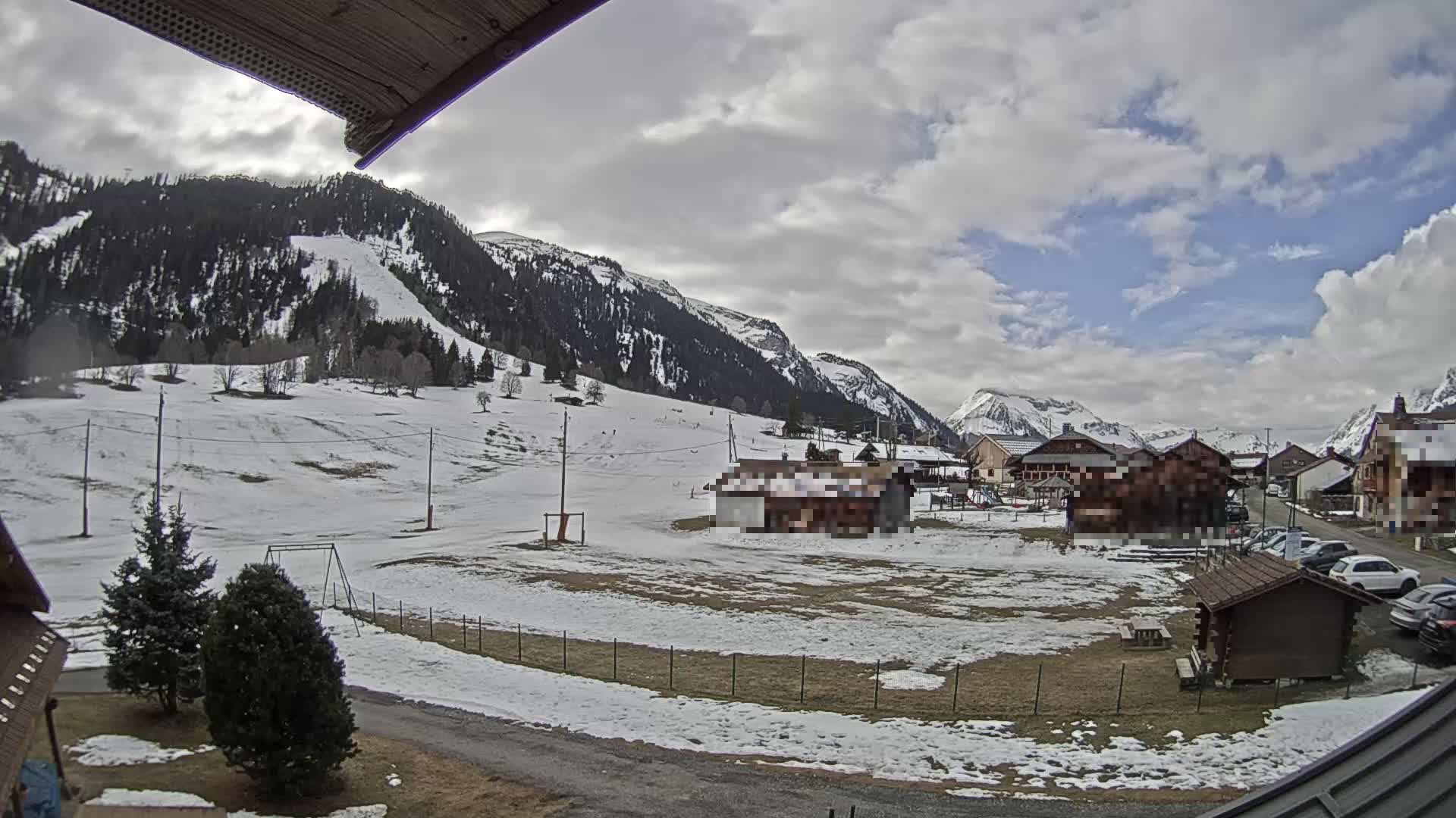 A snow-dusted village nestled in a valley between mountains under a partly cloudy sky.