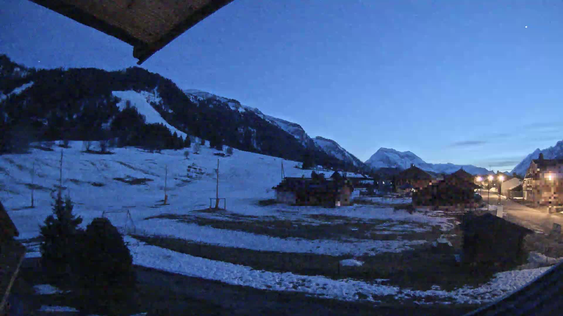 A snow-covered village nestled in a valley between dark mountains under a twilight blue sky.