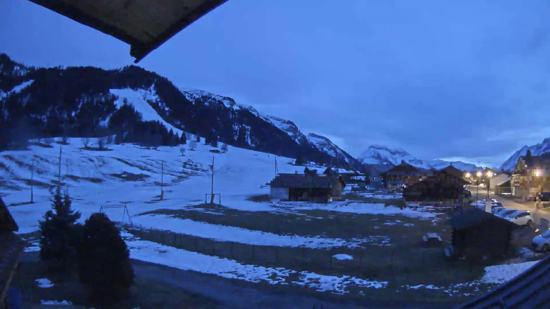A snow-dusted mountain village is nestled in a valley under a twilight sky.