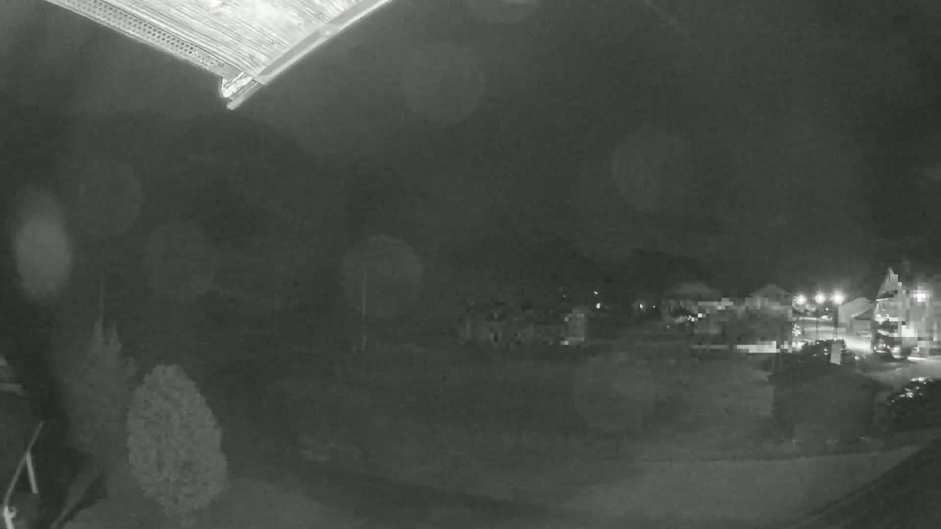A nighttime, low-light view shows a small town or village with some lights visible, partially obscured by what appears to be light rain or snow.