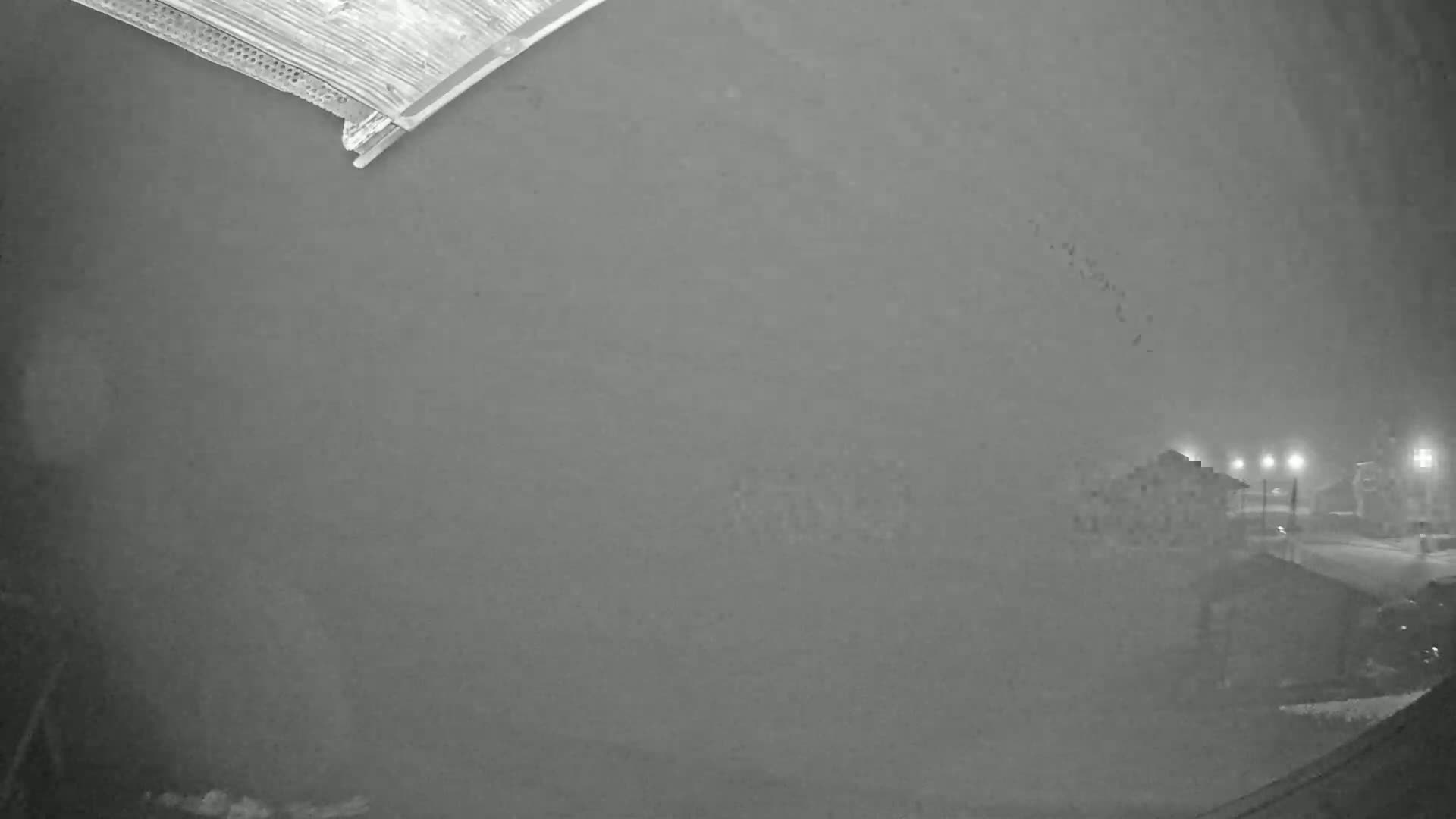 A nighttime view of a snow-covered street with dimly lit buildings in the distance, seen through a blurry, possibly frosted, window.