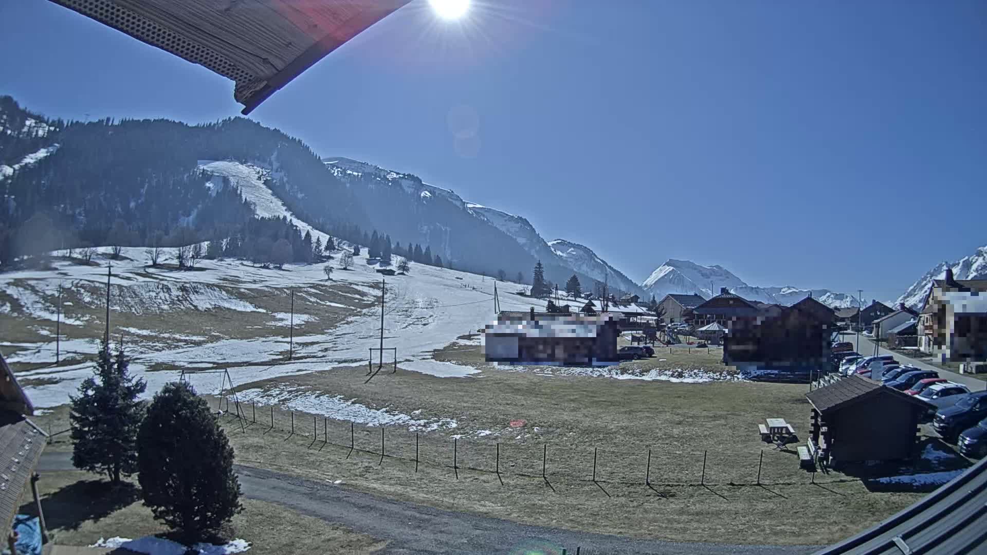 A sunny day in a snow-dusted mountain village, with a view of snow-capped mountains in the background.