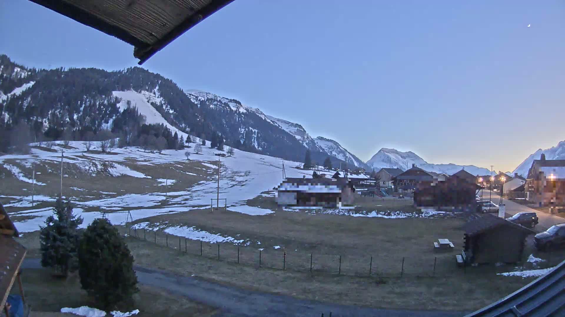 A snow-dusted valley town nestled in the foothills of a mountain range under a twilight sky.