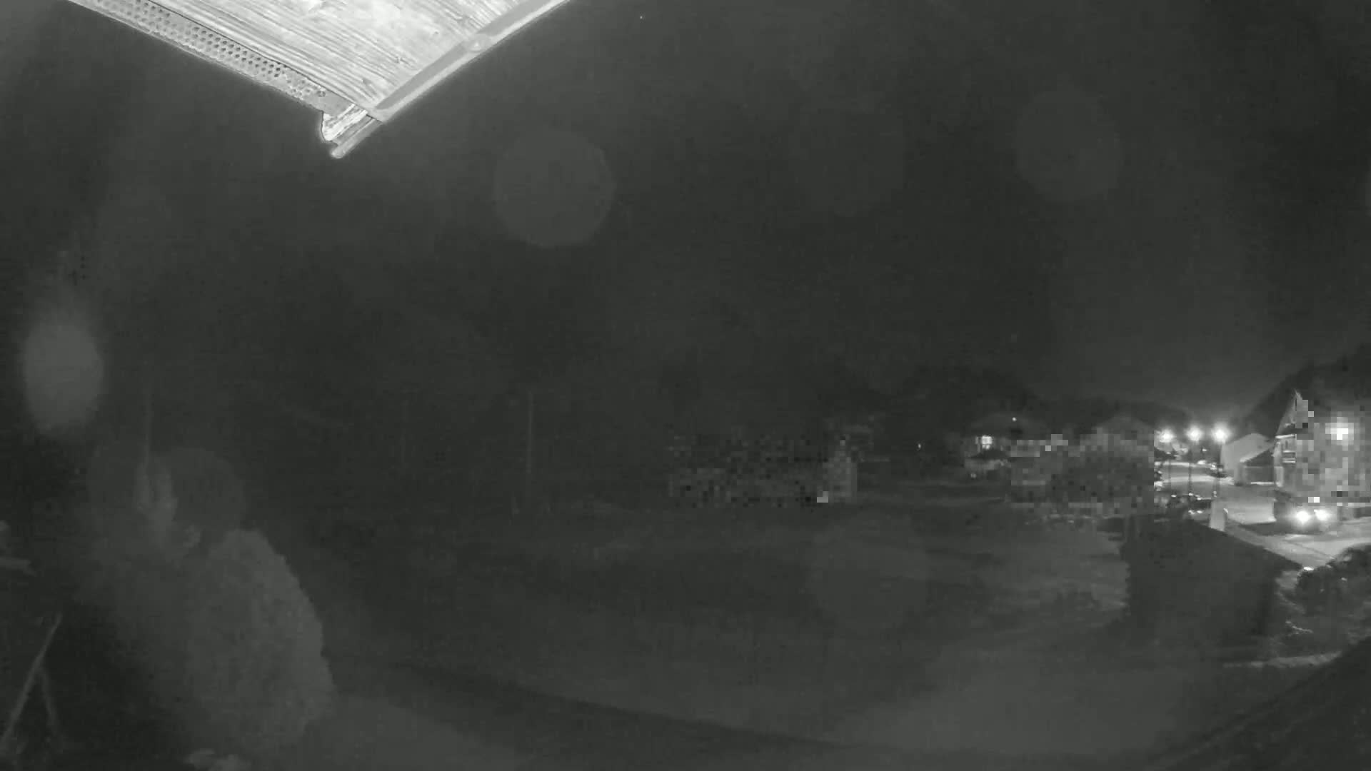 A nighttime, low-light view of a residential area shows several houses and a street with some parked vehicles.