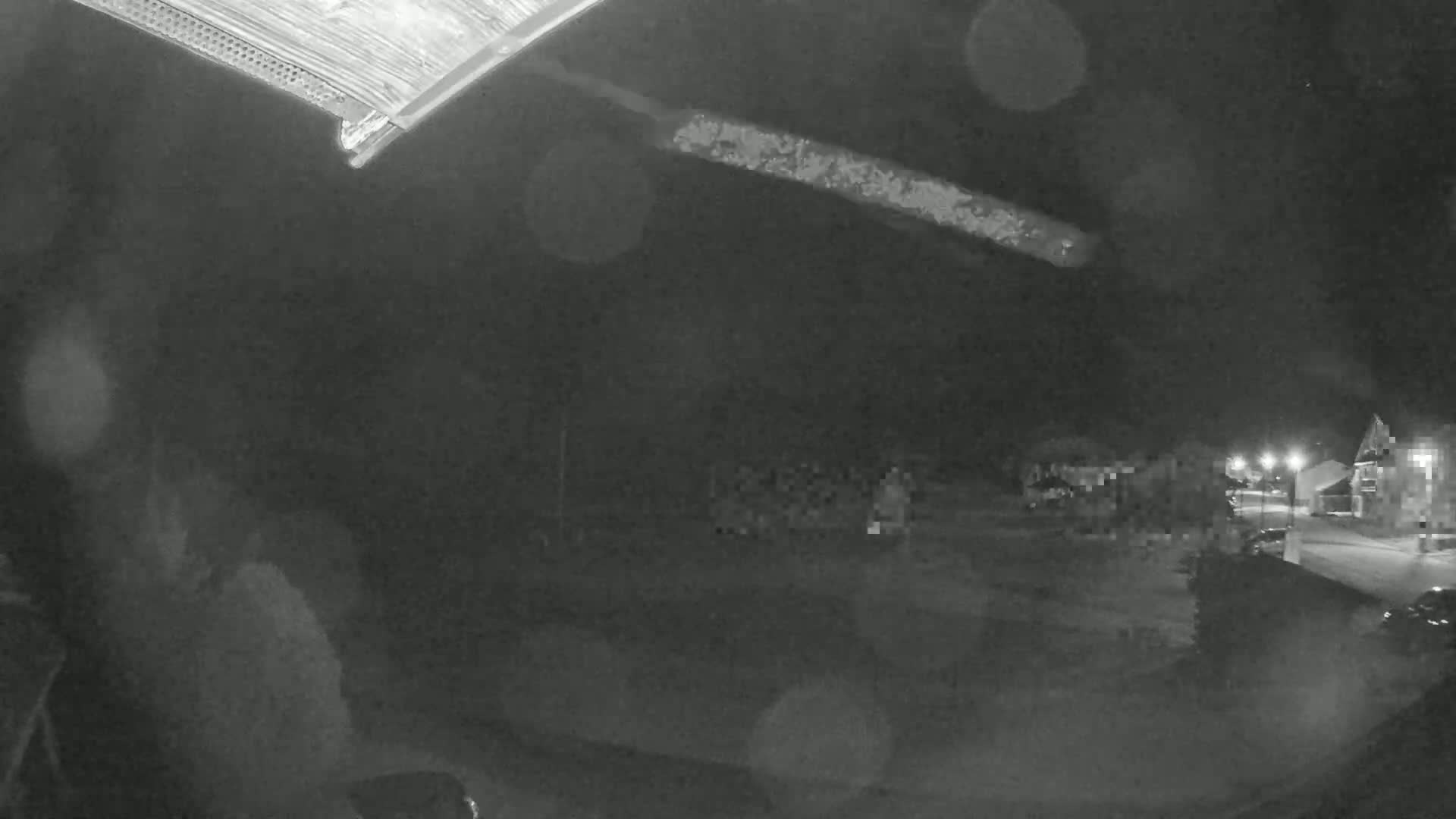 A nighttime, blurry, rain-speckled view shows a street with houses and a long, bright streak across the sky.