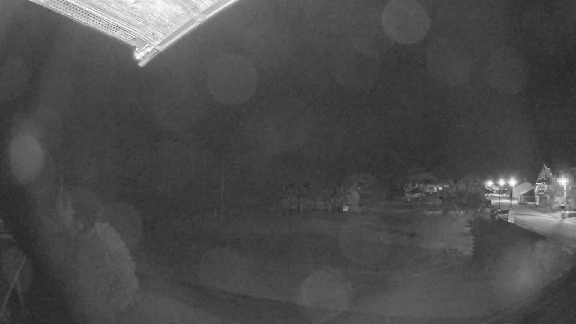 A nighttime, blurry outdoor scene shows a person in the lower left corner, with buildings and streetlights visible in the distance under a dark, possibly rainy sky.