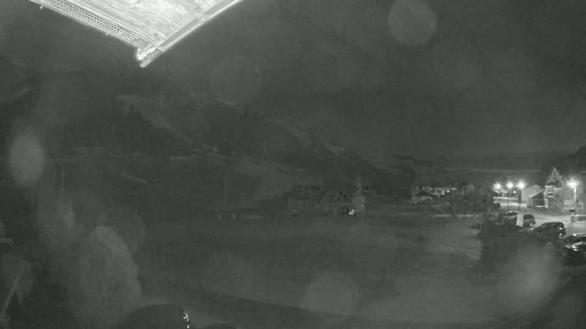 A nighttime, blurry view of a parking lot and buildings under a dark, possibly overcast sky with rain or snow.