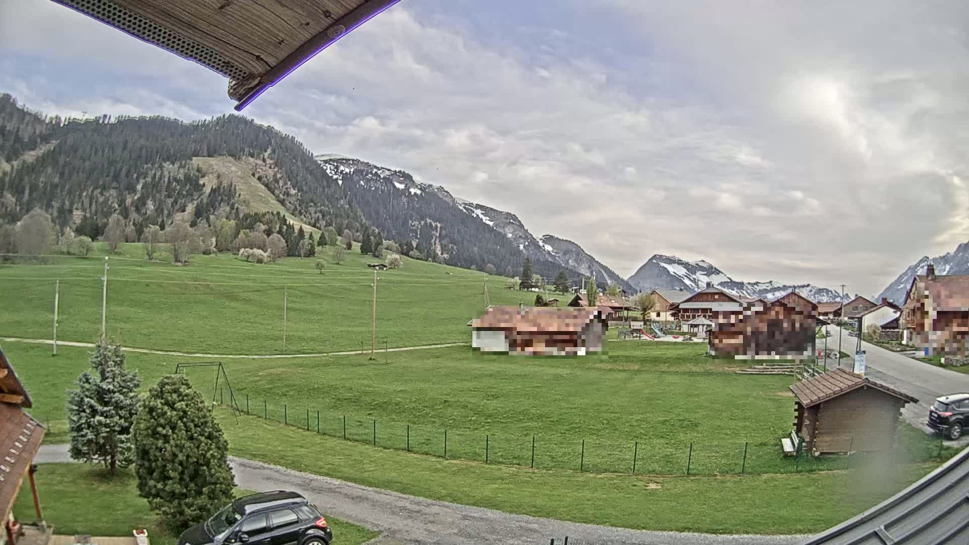 A partly cloudy day shows a green valley with a few buildings and mountains in the background.