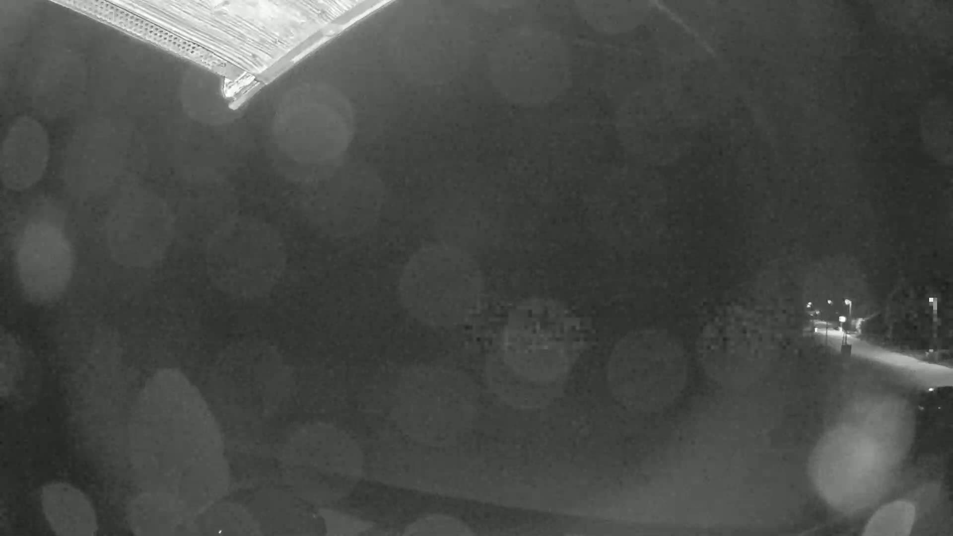 A blurry nighttime image shows a rain-streaked view of a dimly lit road and distant buildings.