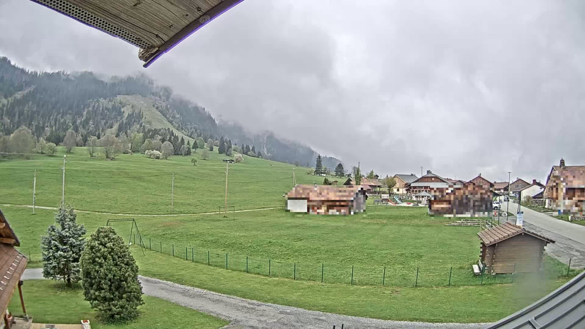 A cloudy day reveals a village nestled in a valley, surrounded by green fields and a misty mountain in the background.