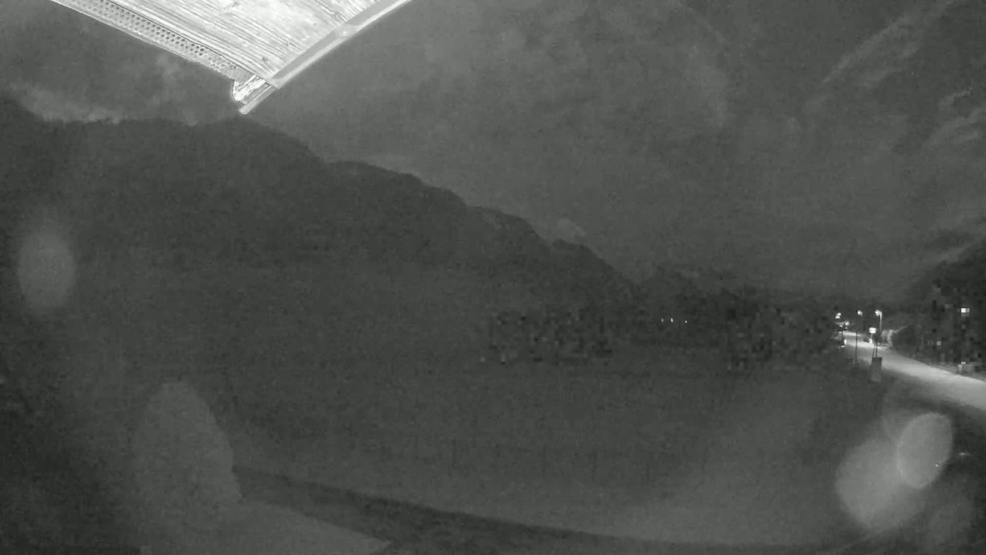 A nighttime, low-light view shows a road leading toward a mountain range under a cloudy sky.