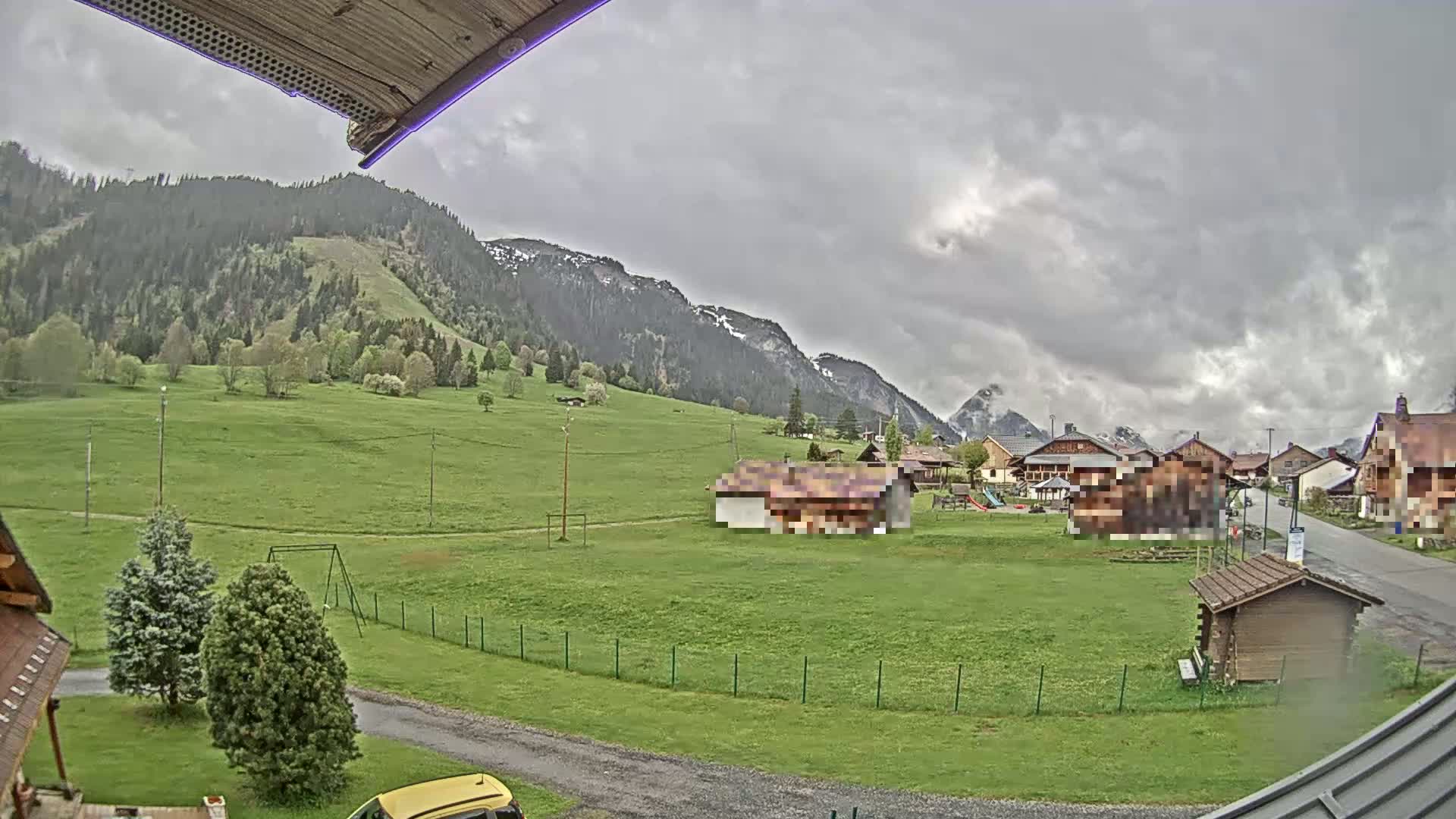 A view of a village nestled in a green valley, with mountains in the background under a cloudy sky.