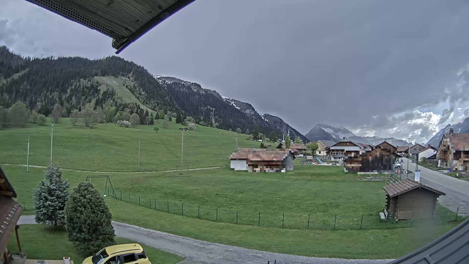 A view of a village nestled in a green valley surrounded by mountains under an overcast sky.