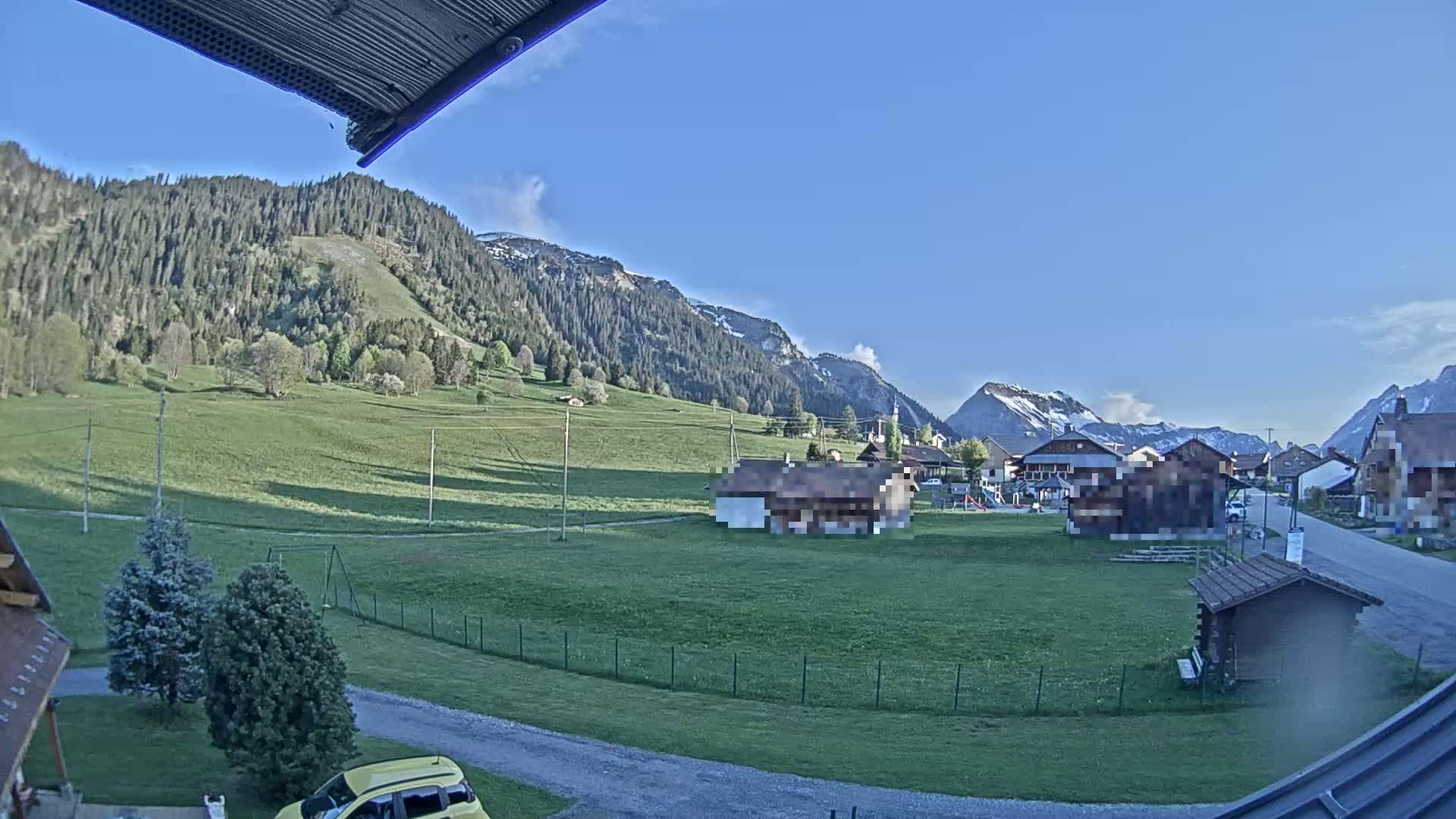 A sunny, clear day reveals a village nestled in a green valley, surrounded by mountains.