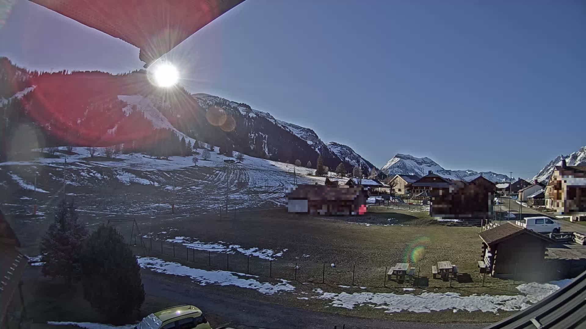 A severe winter whiteout covers a snowy landscape featuring obscured buildings, snow-laden trees, and an icicle dangling from a wooden eave in the foreground.