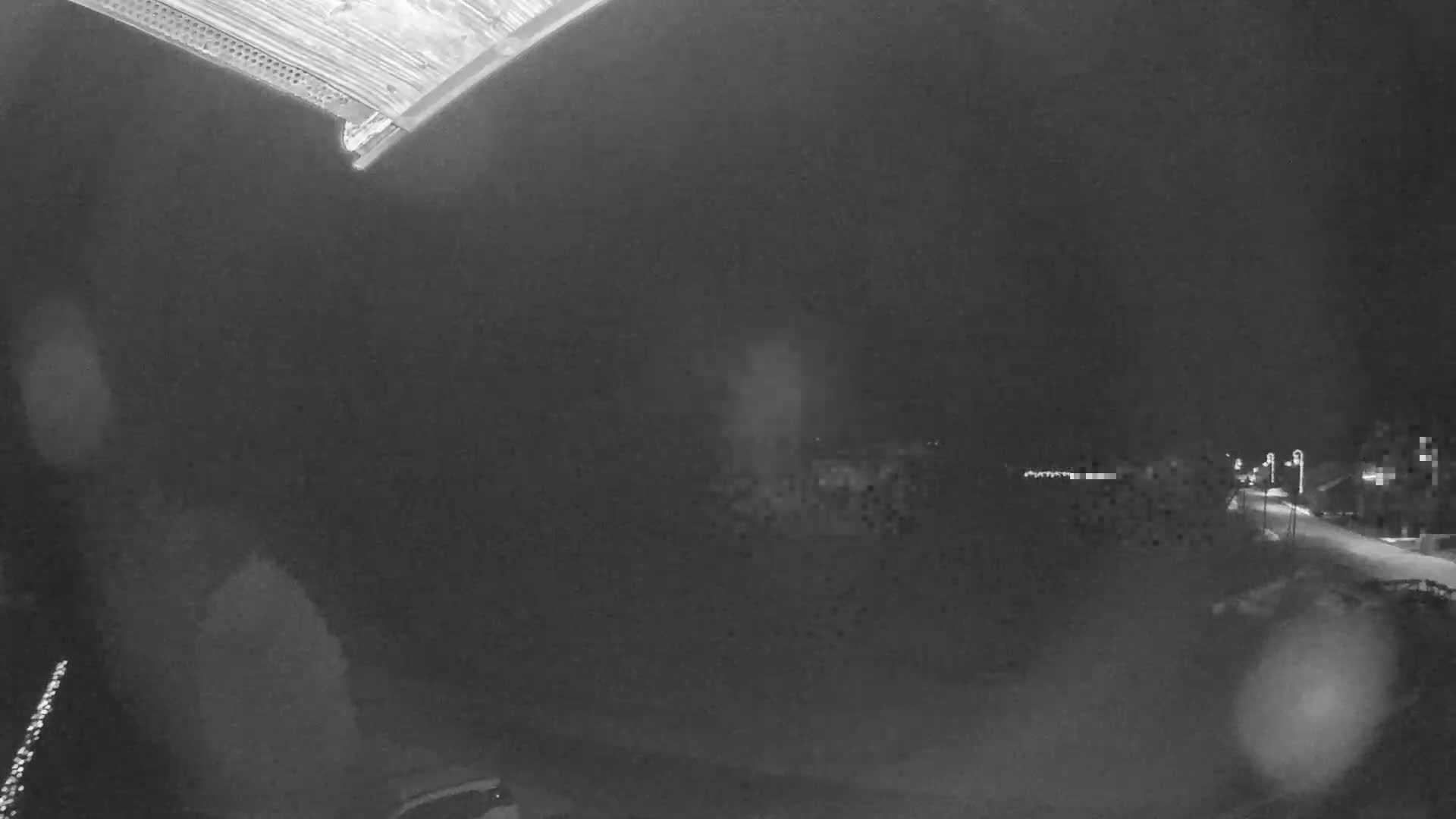 A severe winter whiteout covers a snowy landscape featuring obscured buildings, snow-laden trees, and an icicle dangling from a wooden eave in the foreground.