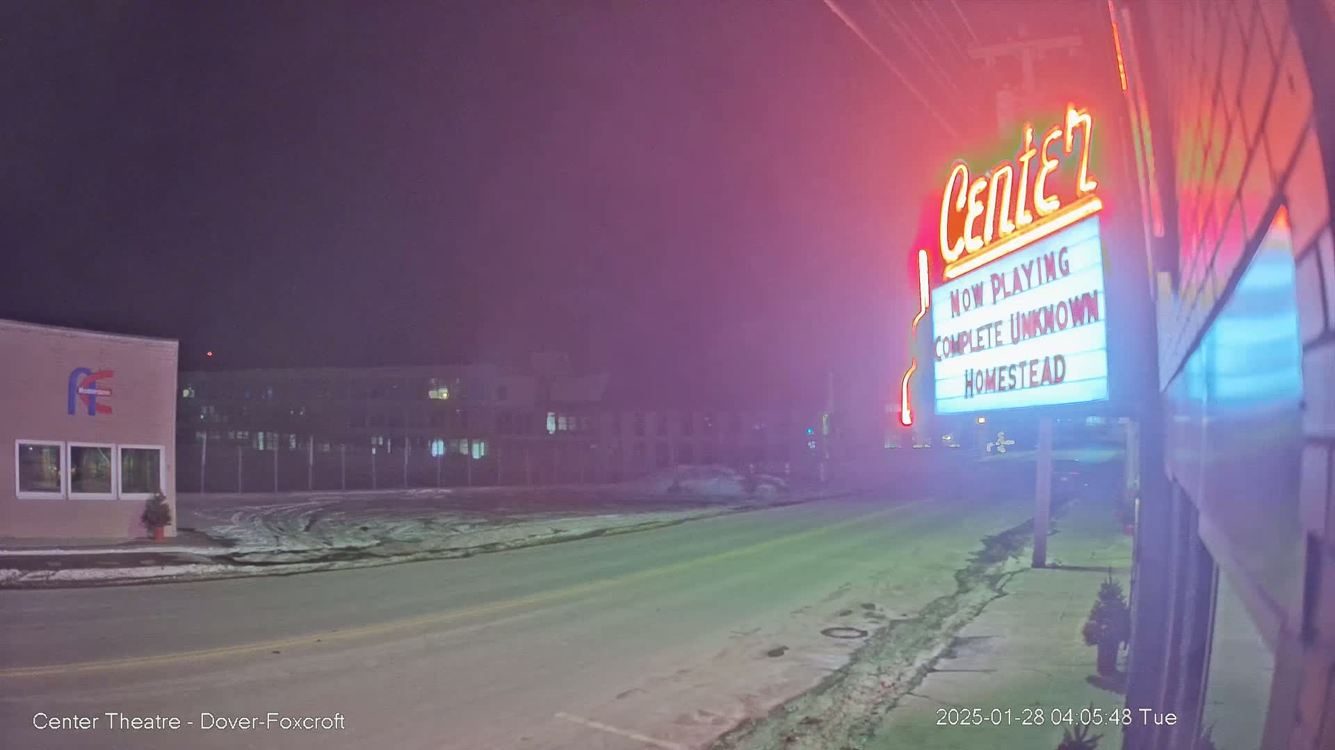 A foggy night scene shows a mostly empty road in front of a movie theater marquee advertising "Complete Unknown" and "Homestead."
