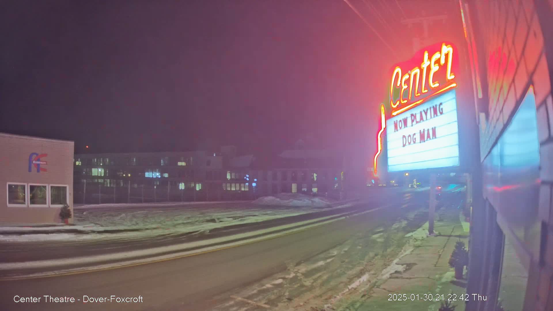 A snowy, foggy night scene shows a movie theater marquee advertising "Dog Man," with buildings and a street visible in the background.