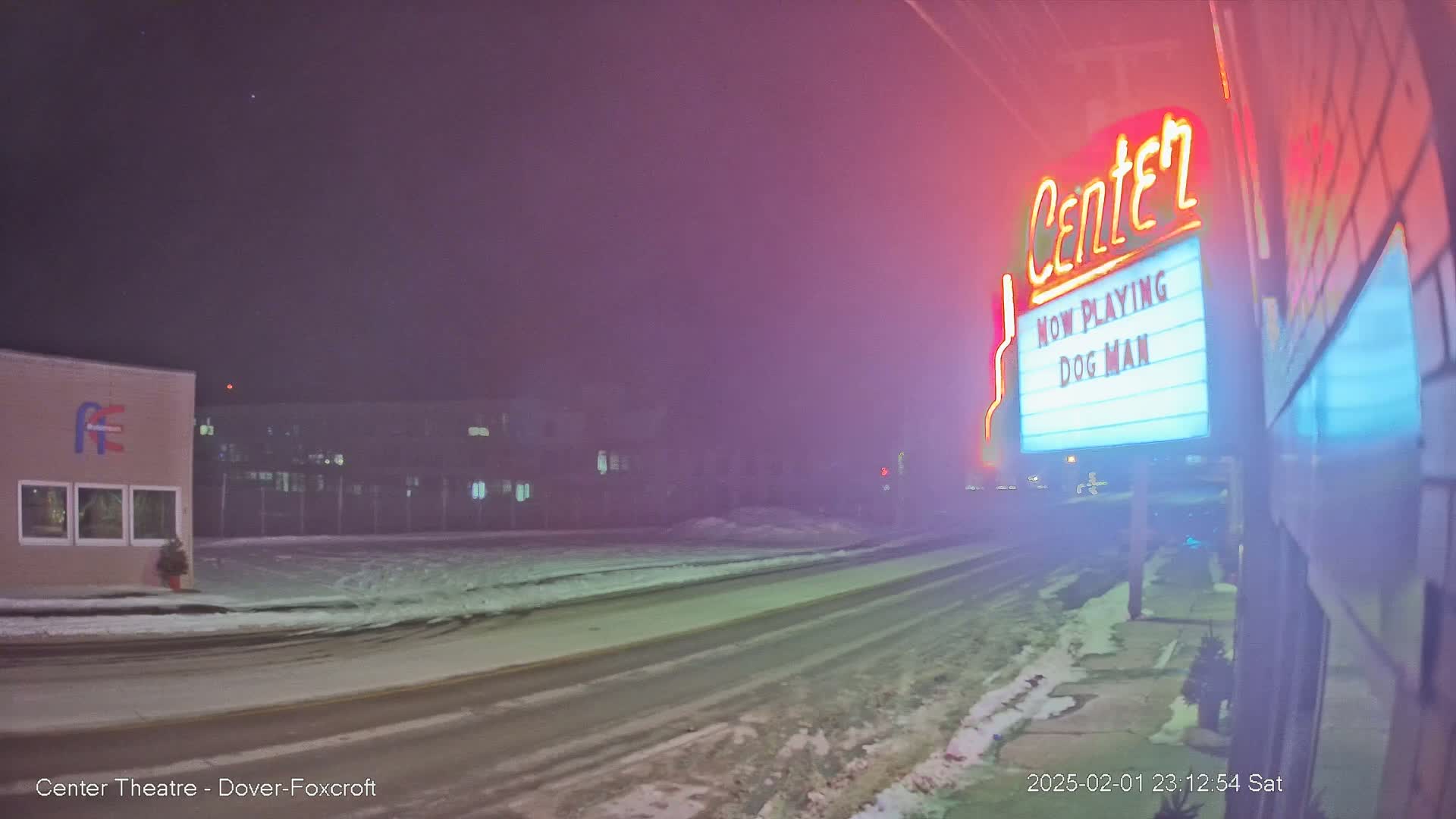 A foggy night scene shows a snow-covered street in front of a movie theater marquee displaying "Dog Man."