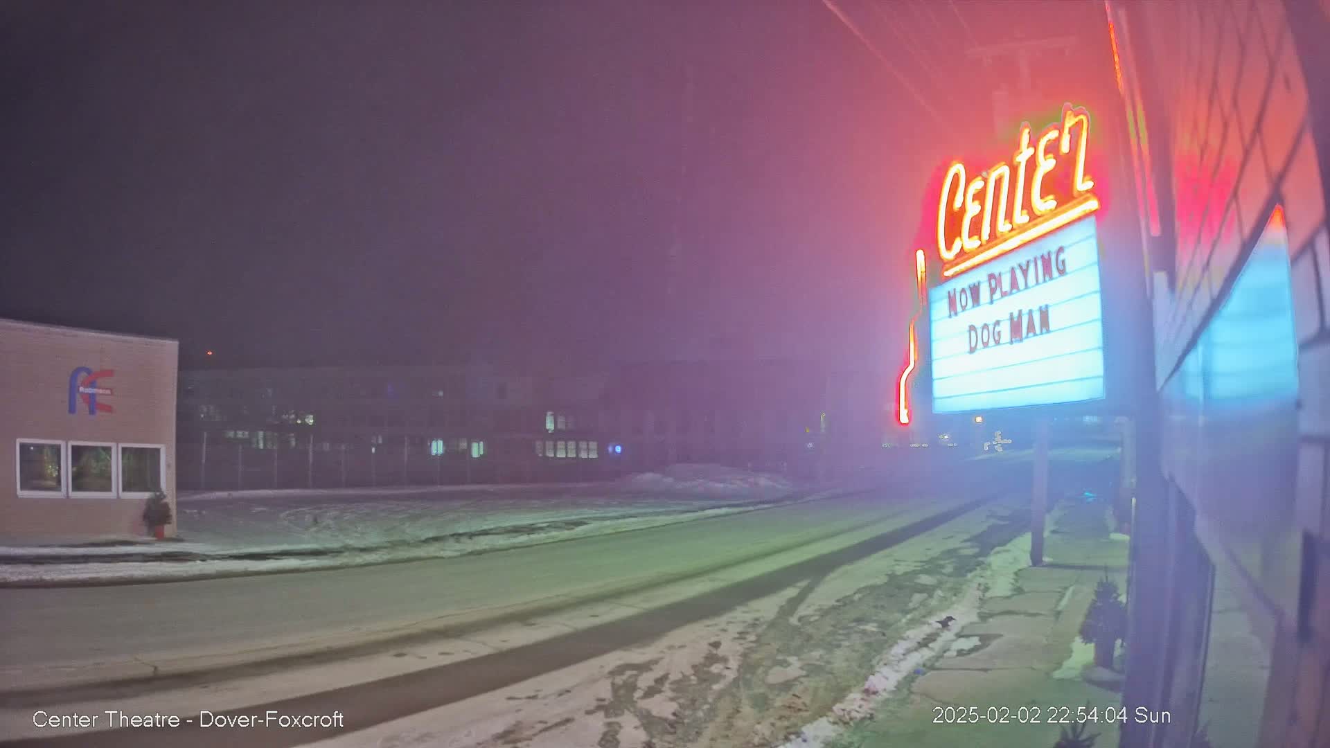 A foggy night scene shows a snow-covered road leading to a movie theater marquee advertising "Dog Man."