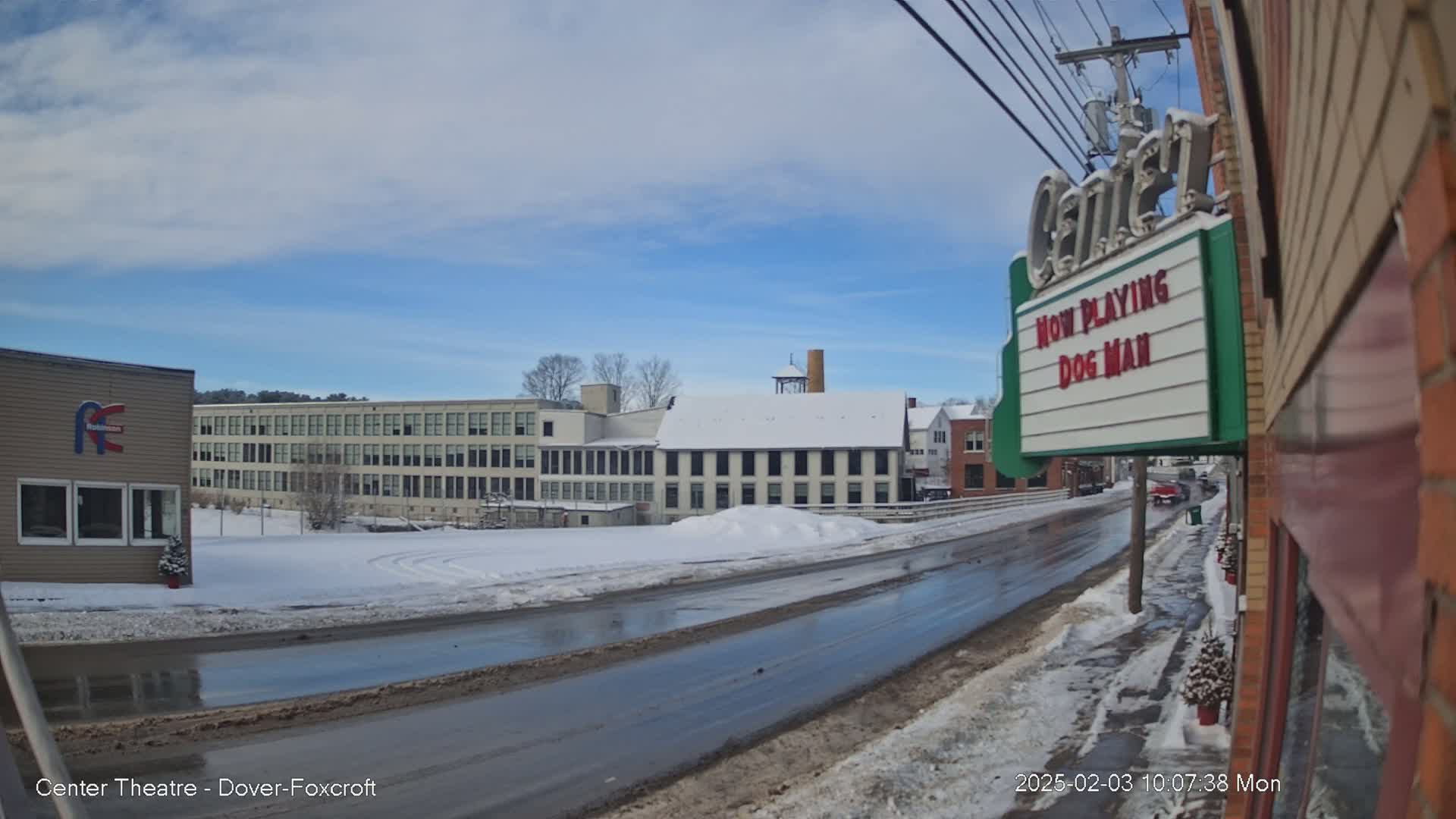 A snow-covered street scene shows a wet road, several buildings including a large mill, and a movie theater marquee advertising "Dog Man."