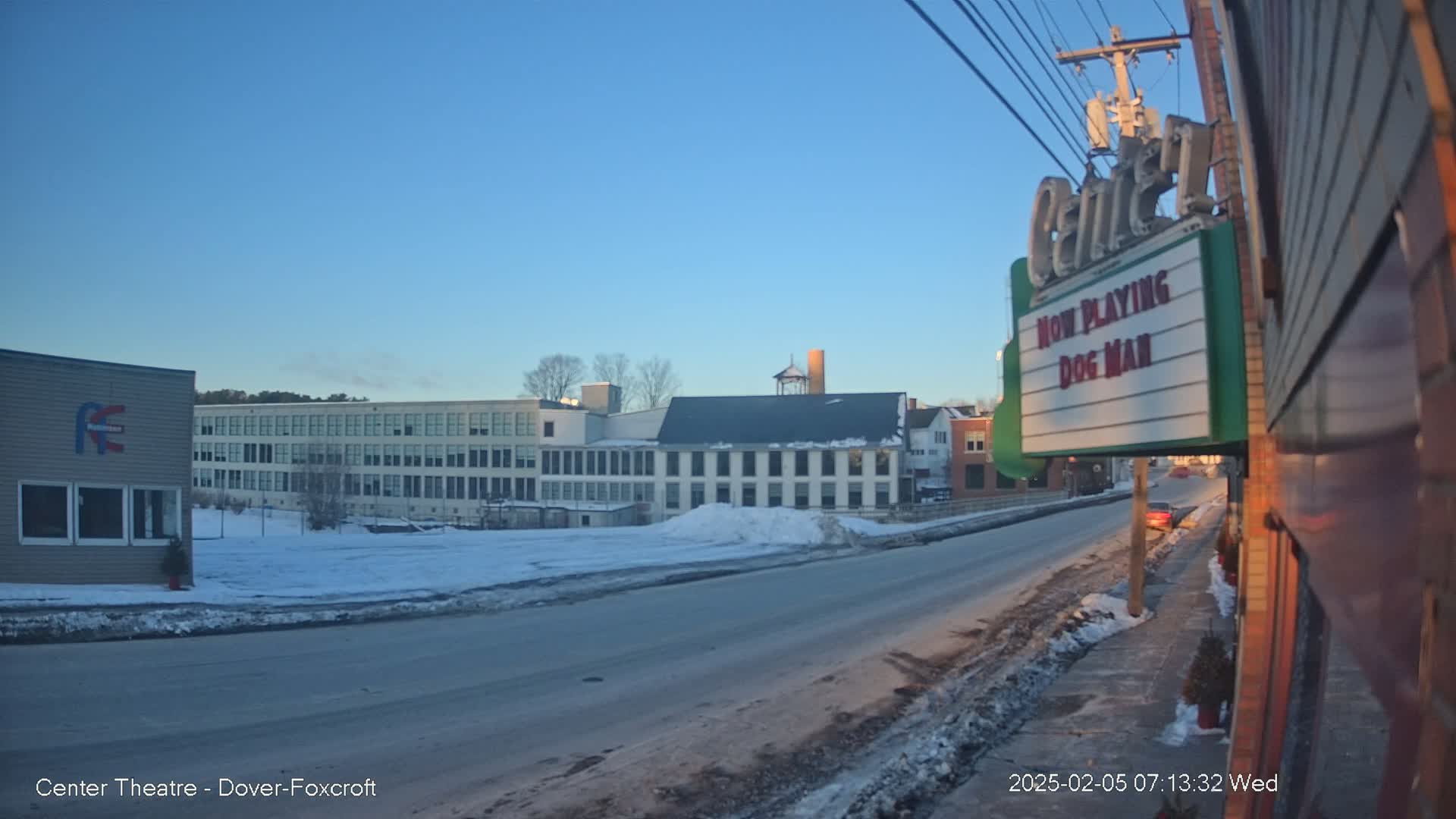 A snow-covered street scene shows several buildings under a clear blue sky, with a marquee displaying "Dog Man."