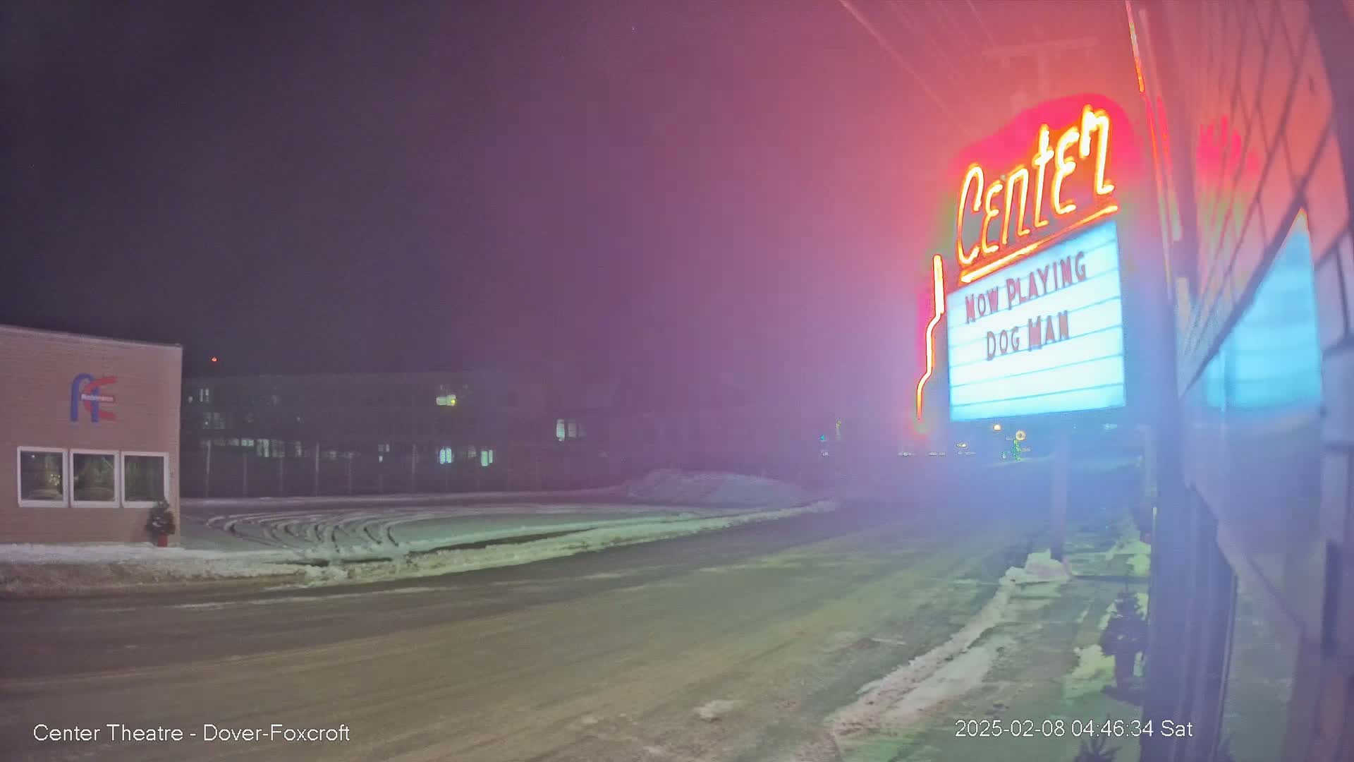 A snowy, foggy street at night shows a movie theater marquee advertising "Dog Man."