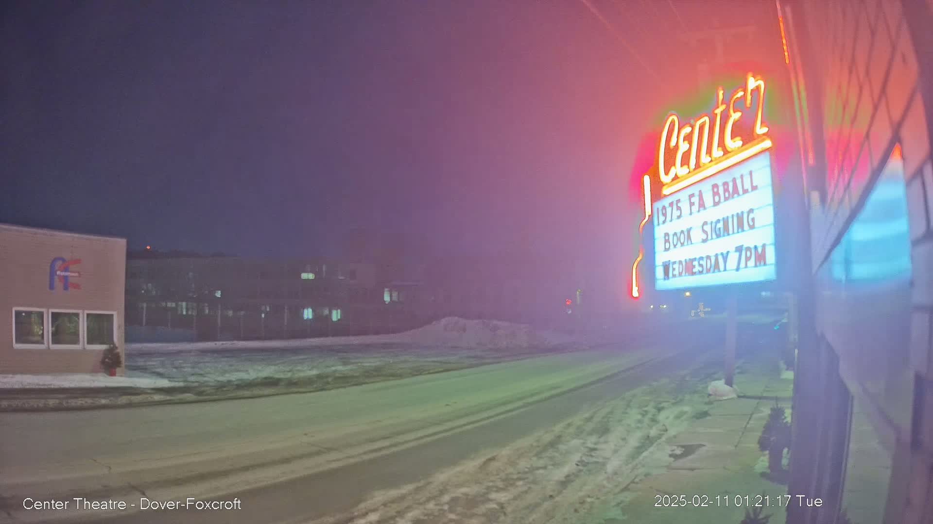 A foggy night scene shows a snow-covered street in front of a building with a neon sign advertising a book signing.