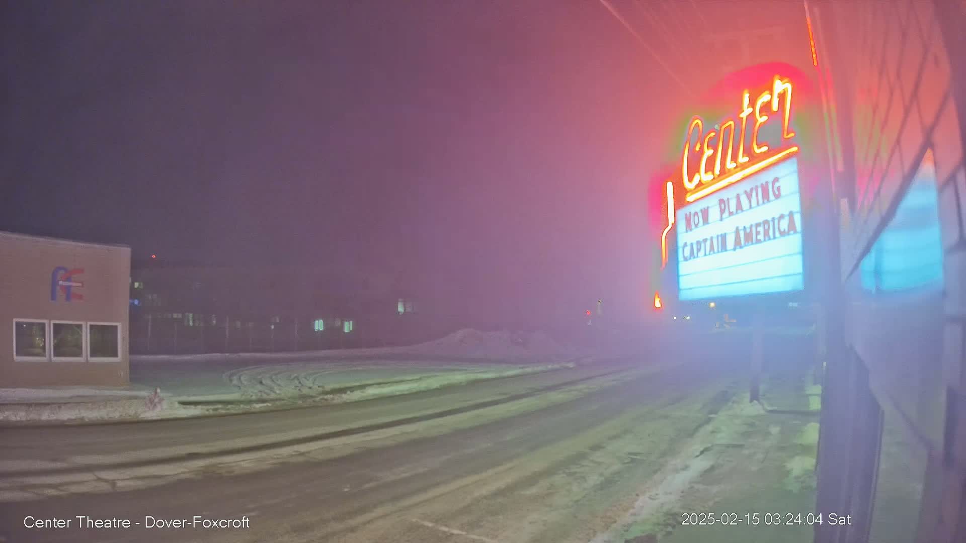 A foggy night scene shows a snow-covered street in front of a movie theater marquee displaying "Captain America."