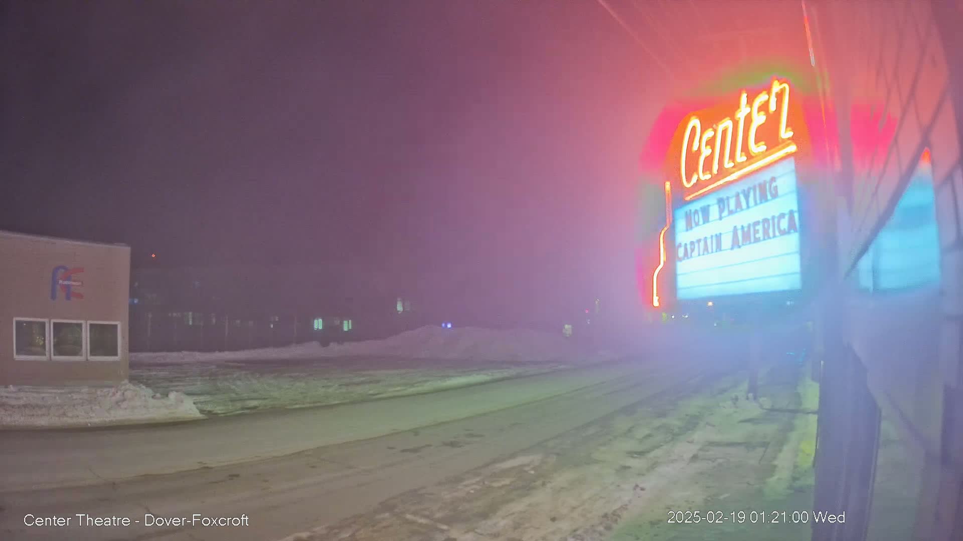 A foggy night scene shows a movie theater marquee advertising "Captain America," with a snow-covered street and buildings in the background.