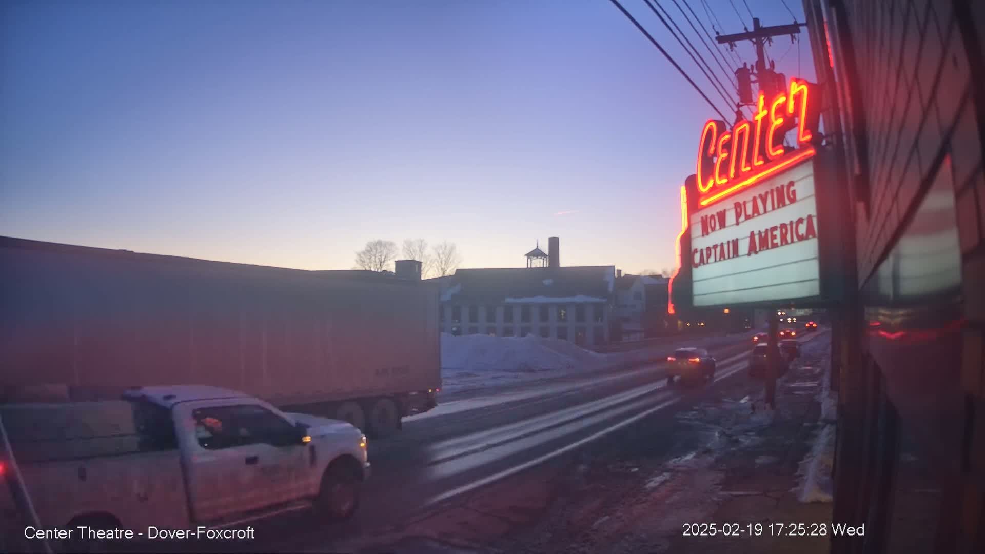 A twilight scene shows a snowy road with a pickup truck and semi-truck driving past a movie theater marquee advertising "Captain America."