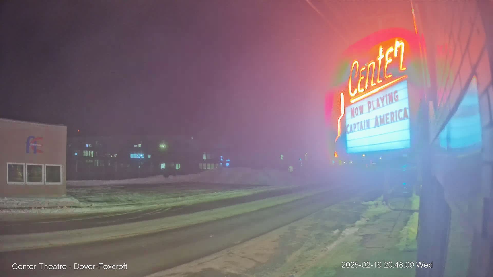 A snowy, foggy night scene shows a movie theater marquee advertising "Captain America," with buildings and a road visible in the distance.