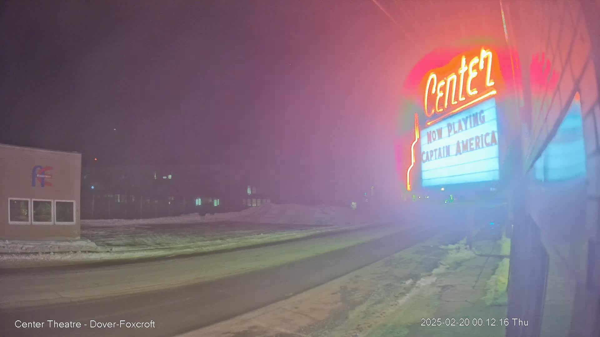 A foggy night scene shows a movie theater marquee advertising Captain America, with a road and snow-covered ground in the foreground.