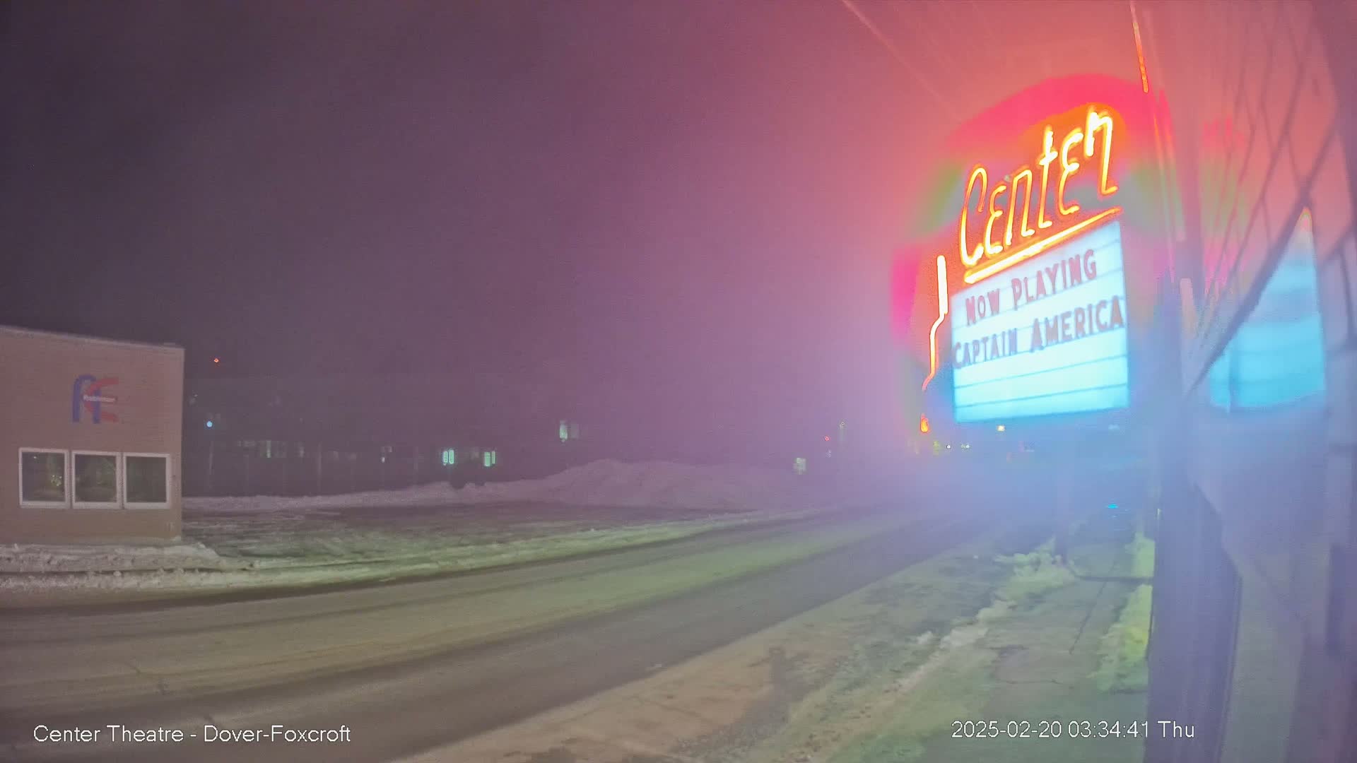 A nighttime, snowy scene shows a road leading to a movie theater marquee displaying "Captain America."