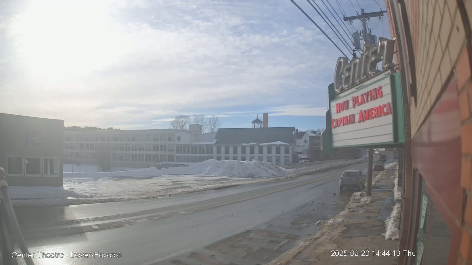 A sunny winter day shows a snow-covered street scene with buildings, including a school and a theater marquee advertising "Captain America."