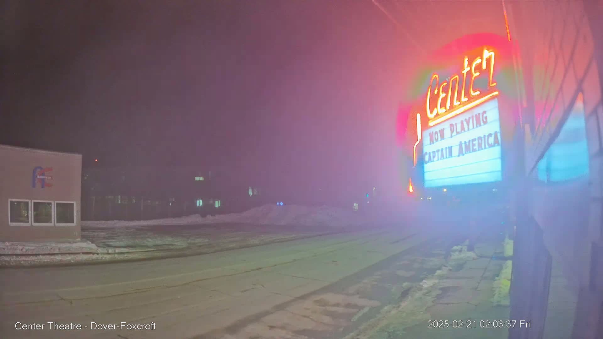 A foggy night scene shows a movie theater marquee advertising "Captain America," with a snow-covered street in front.