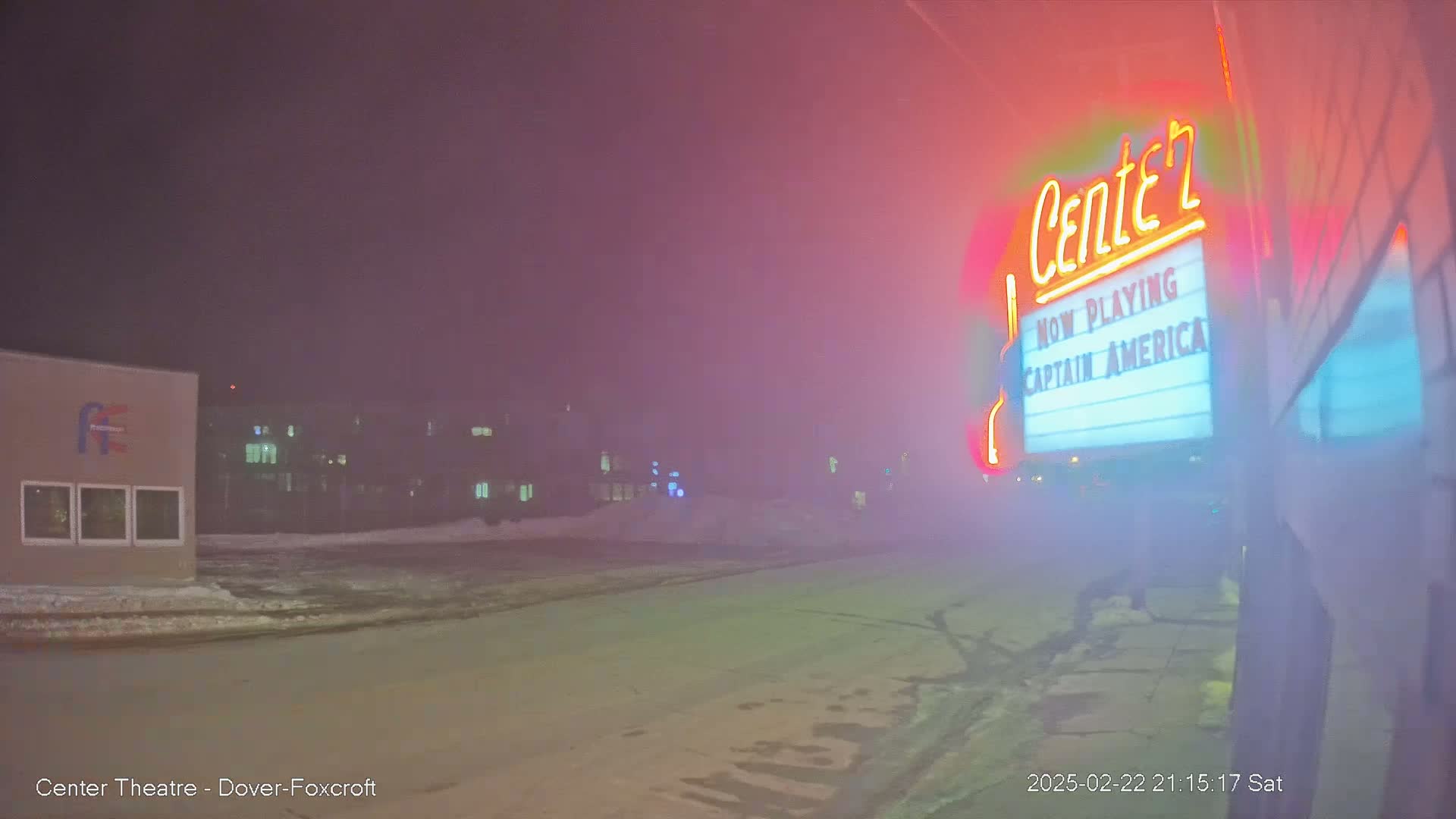 A foggy night scene shows a movie theater marquee advertising Captain America, with a snow-covered street and buildings in the background.