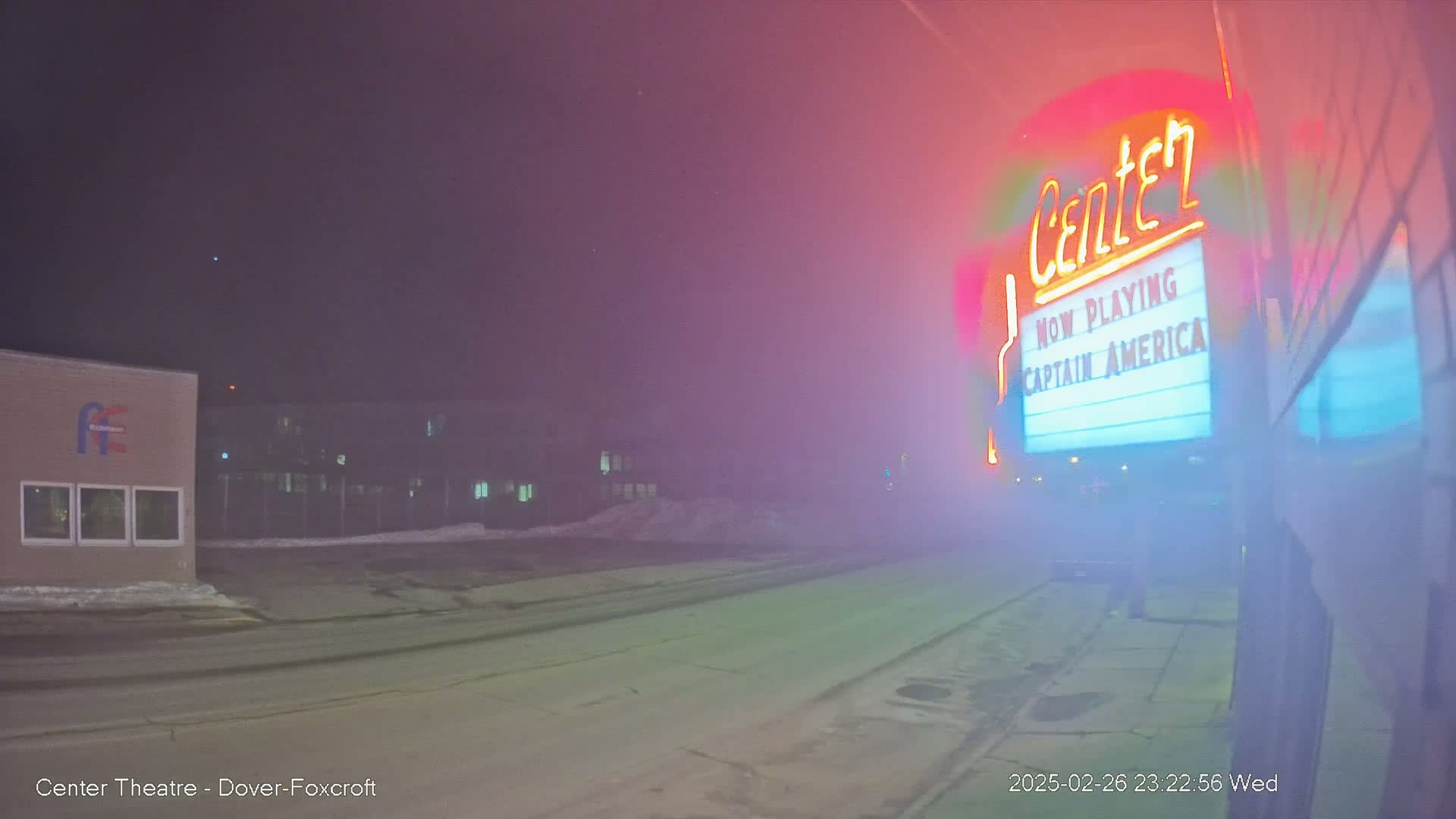 A foggy night scene shows a movie theater marquee advertising "Captain America," with a building and a road visible in the background.